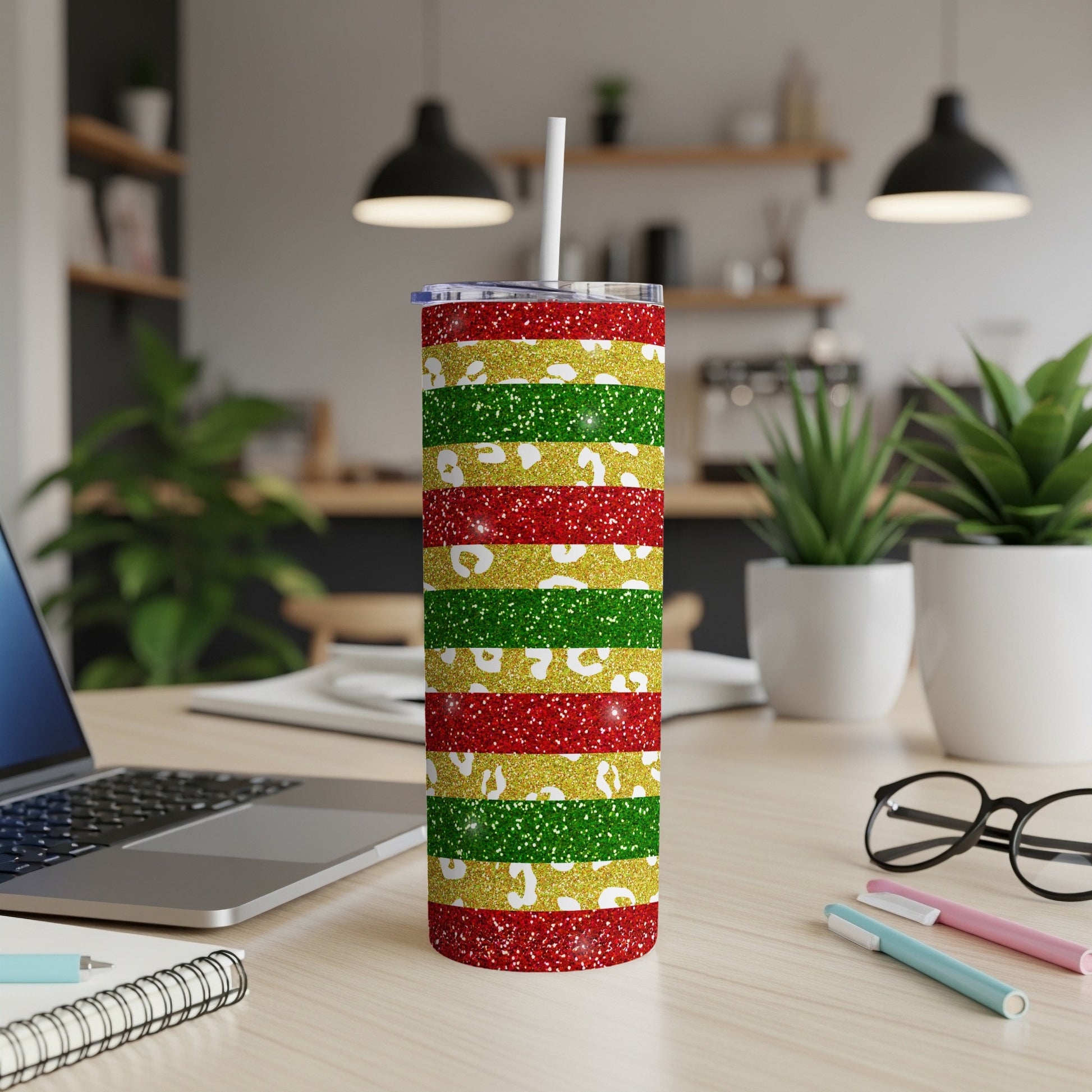 Glittery red, green, and gold striped tumbler with straw on a desk.