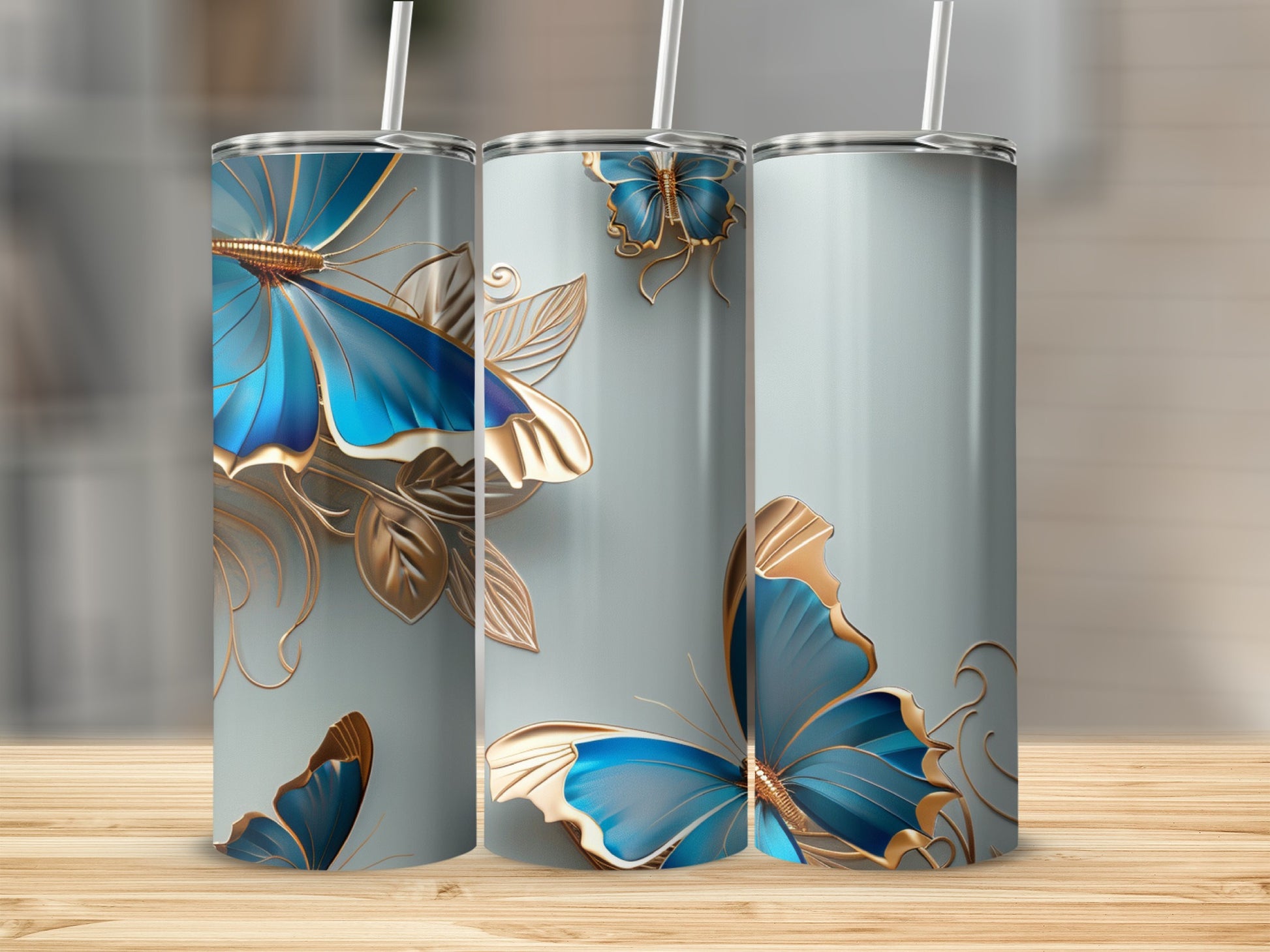 Three tumblers with blue butterflies and gold accents on a wooden surface.