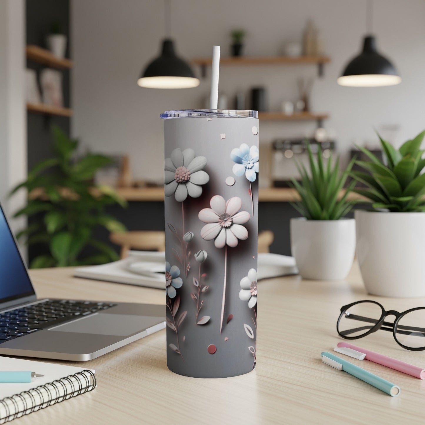 Gray floral tumbler with a straw on a desk with a laptop and pens.