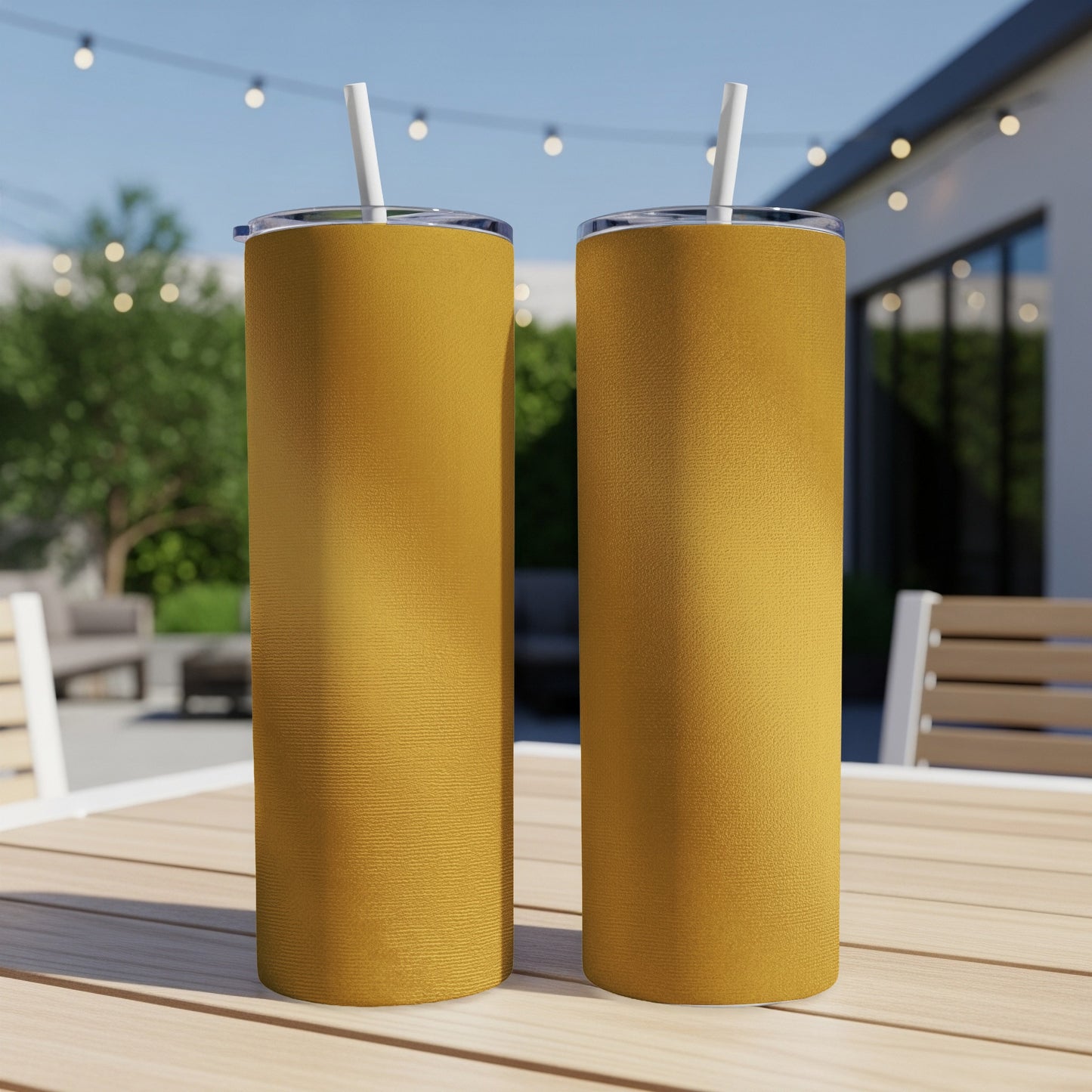 Two gold tumblers with white straws sit on a wooden table outdoors.