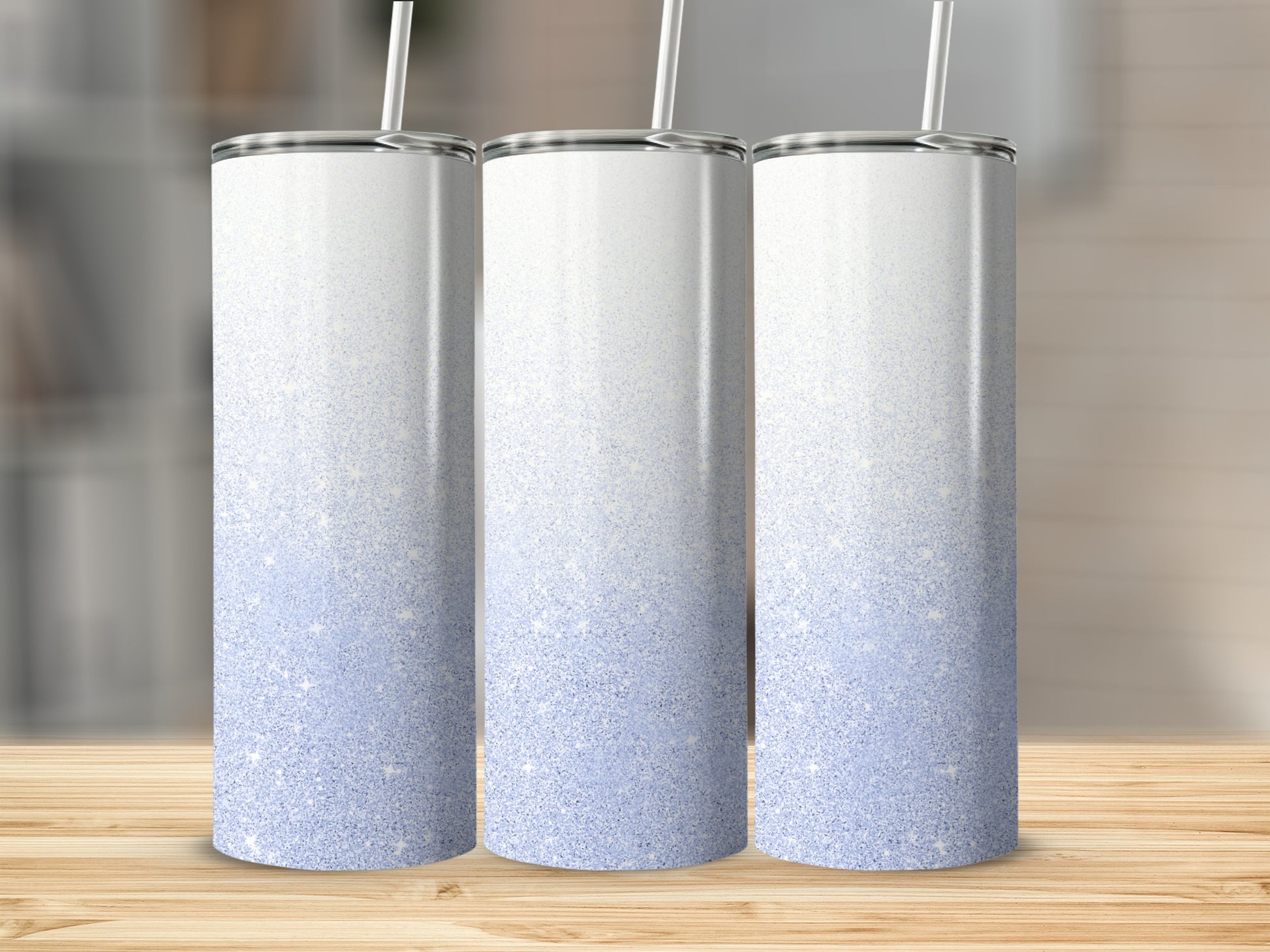Three white tumblers with blue glitter ombre design on a wooden surface.