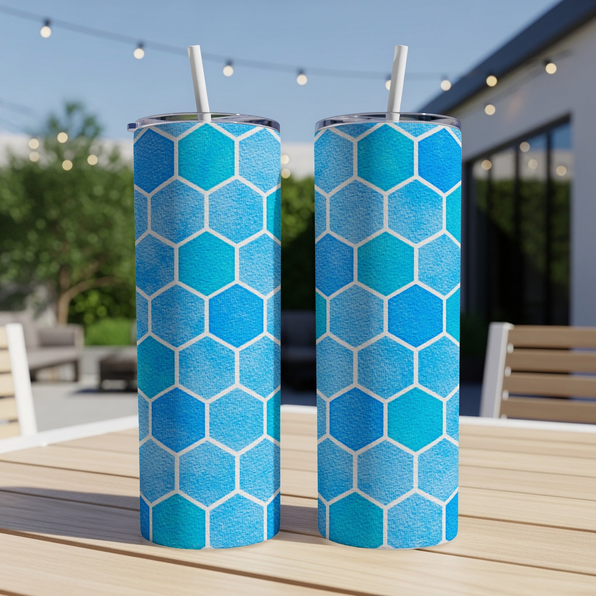 Two tumblers with a blue hexagon pattern and white straws on a wooden table.