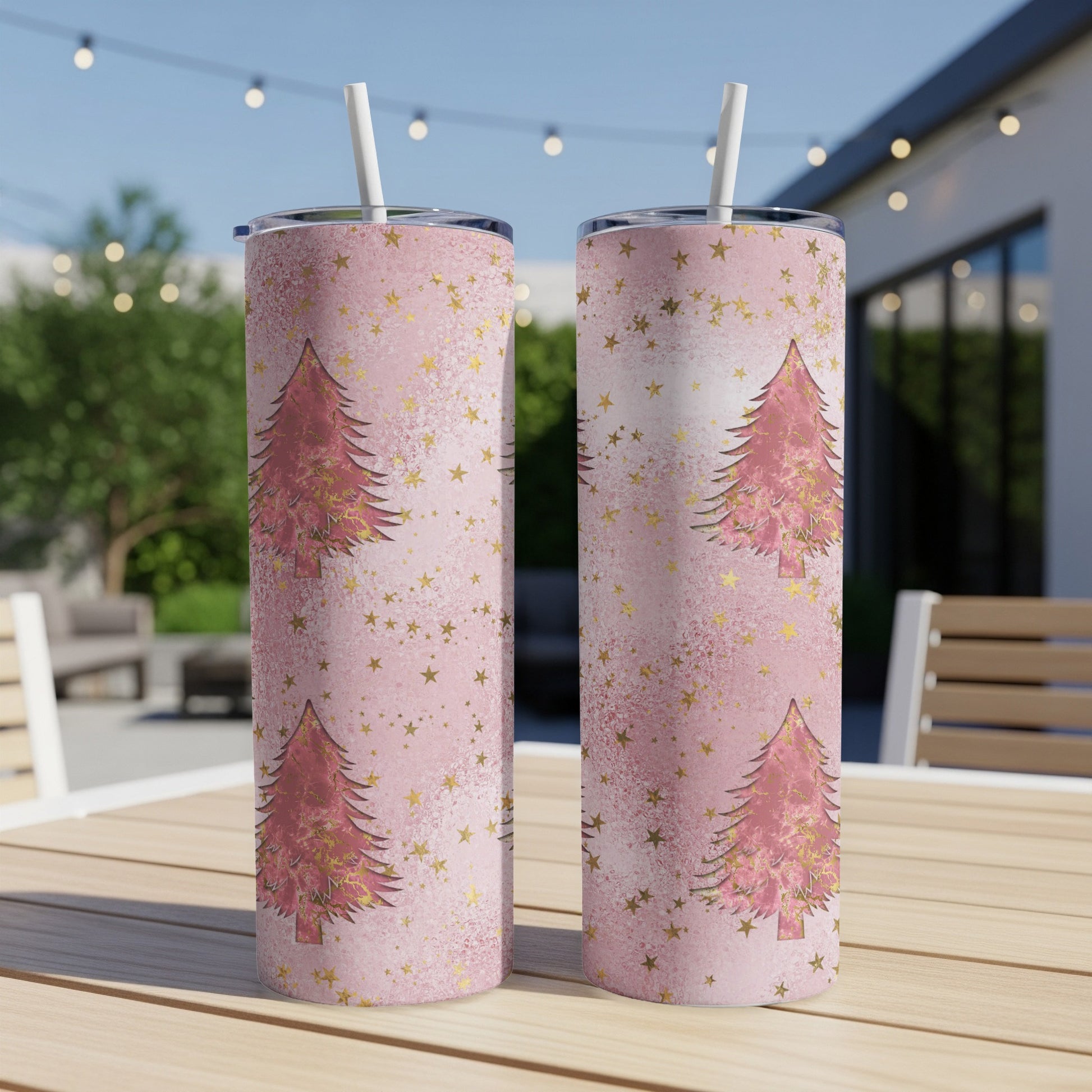 Two pink tumblers with gold stars and Christmas trees on a table.