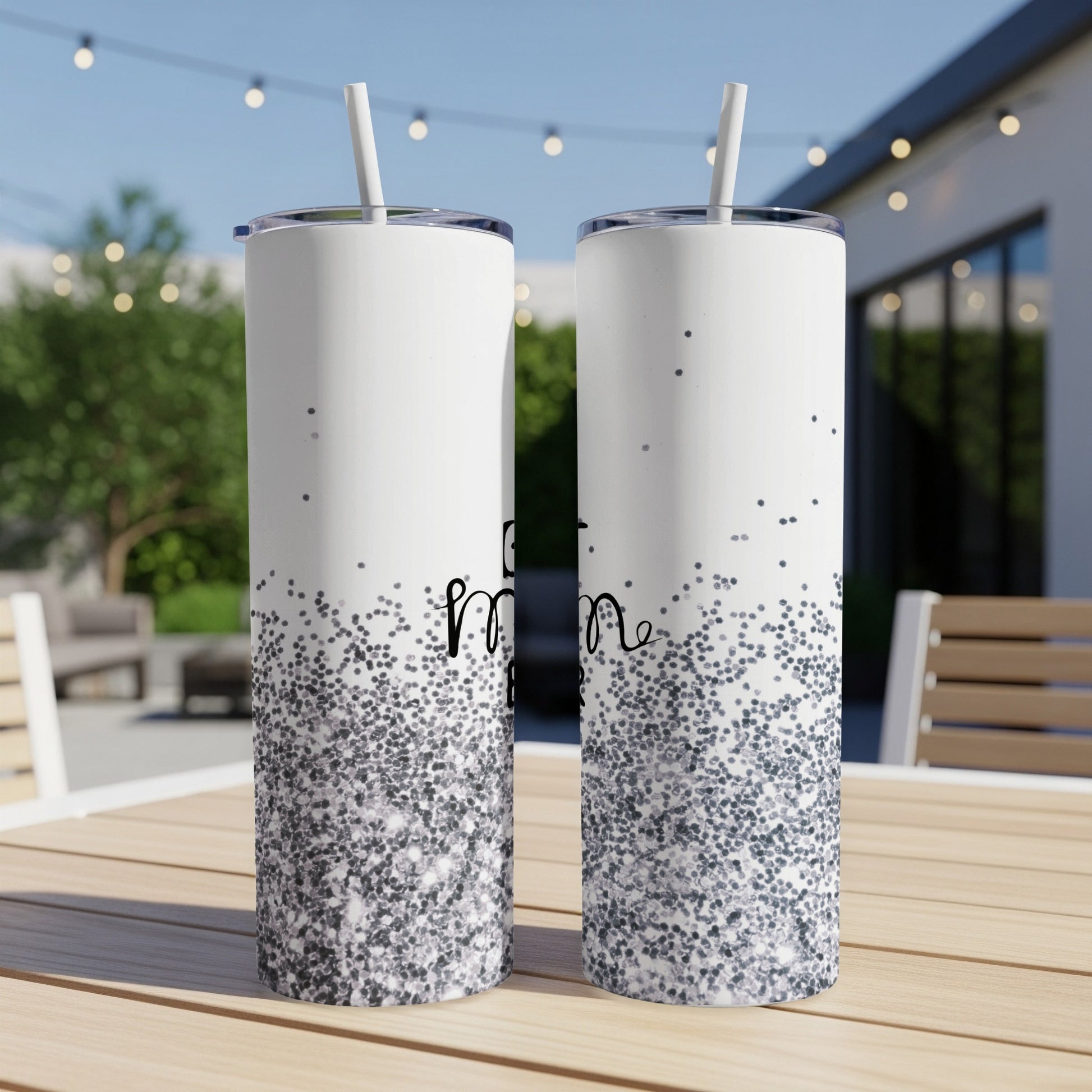 Two white tumblers with "best mom" text and glitter design on a table.