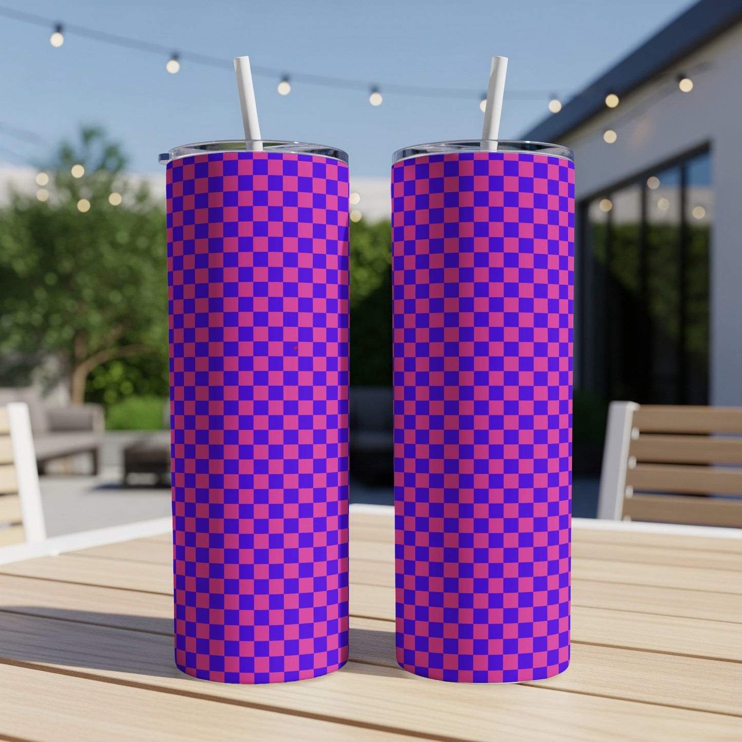 Two purple and pink checkered tumblers with straws on a table.