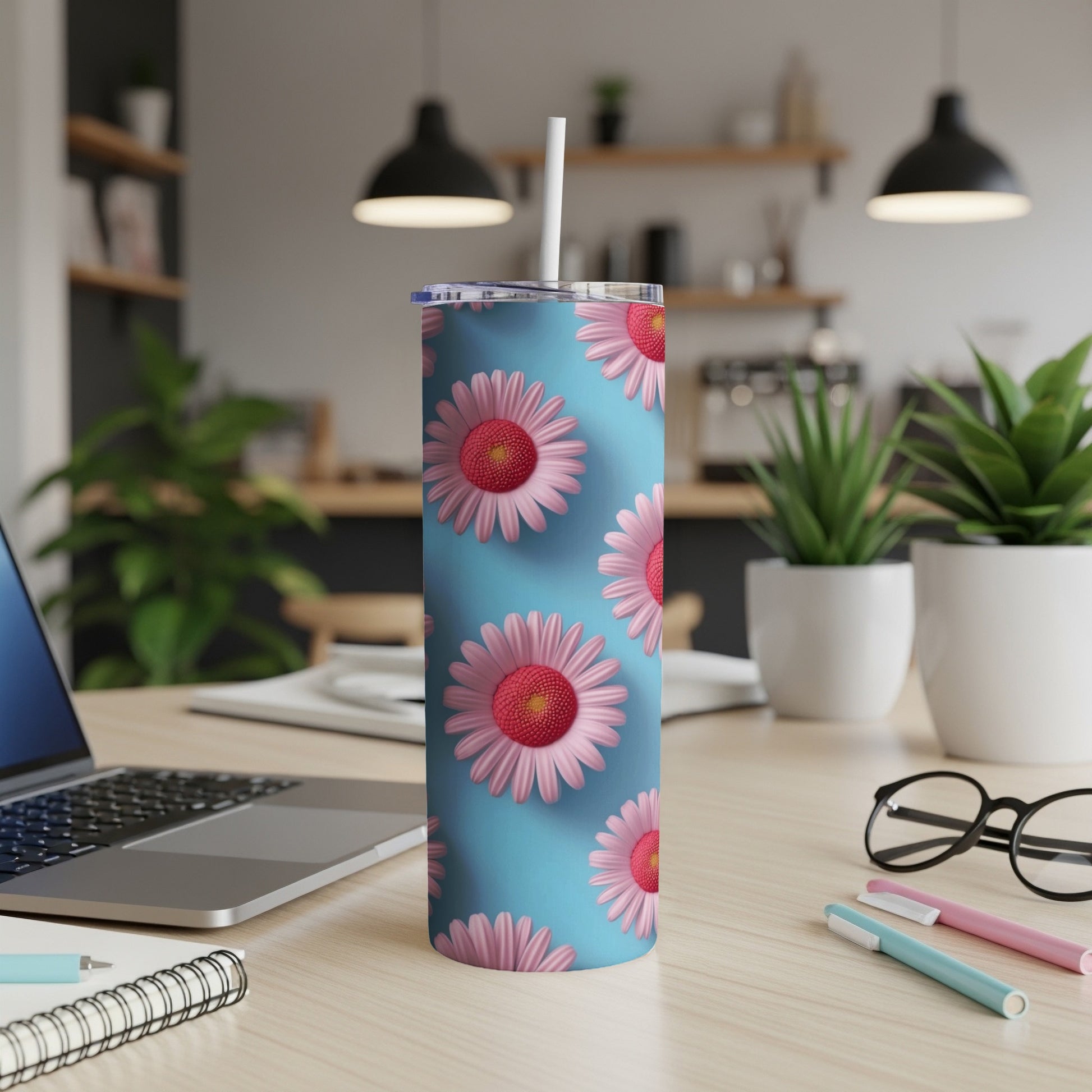 Blue tumbler with pink and red daisies, sitting on a desk.
