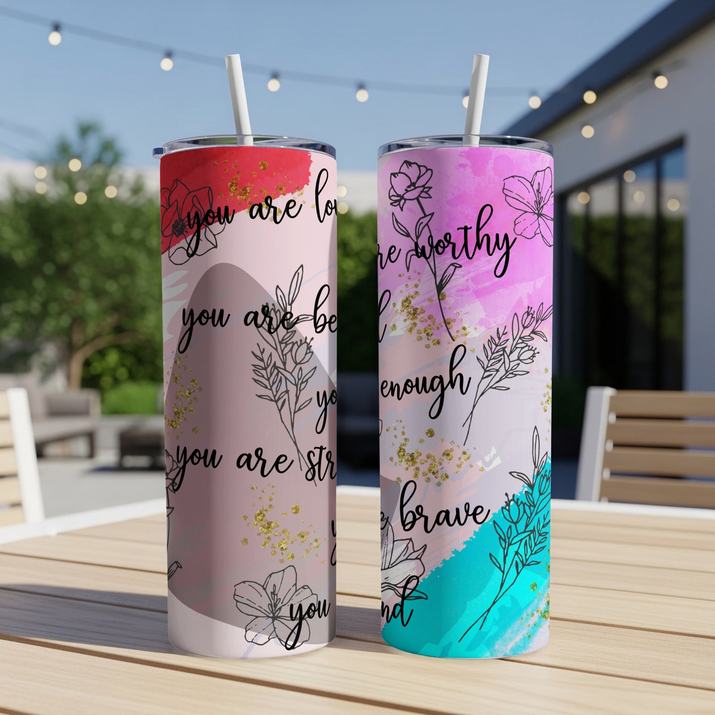 Two tumblers with floral designs and inspirational text on a table.