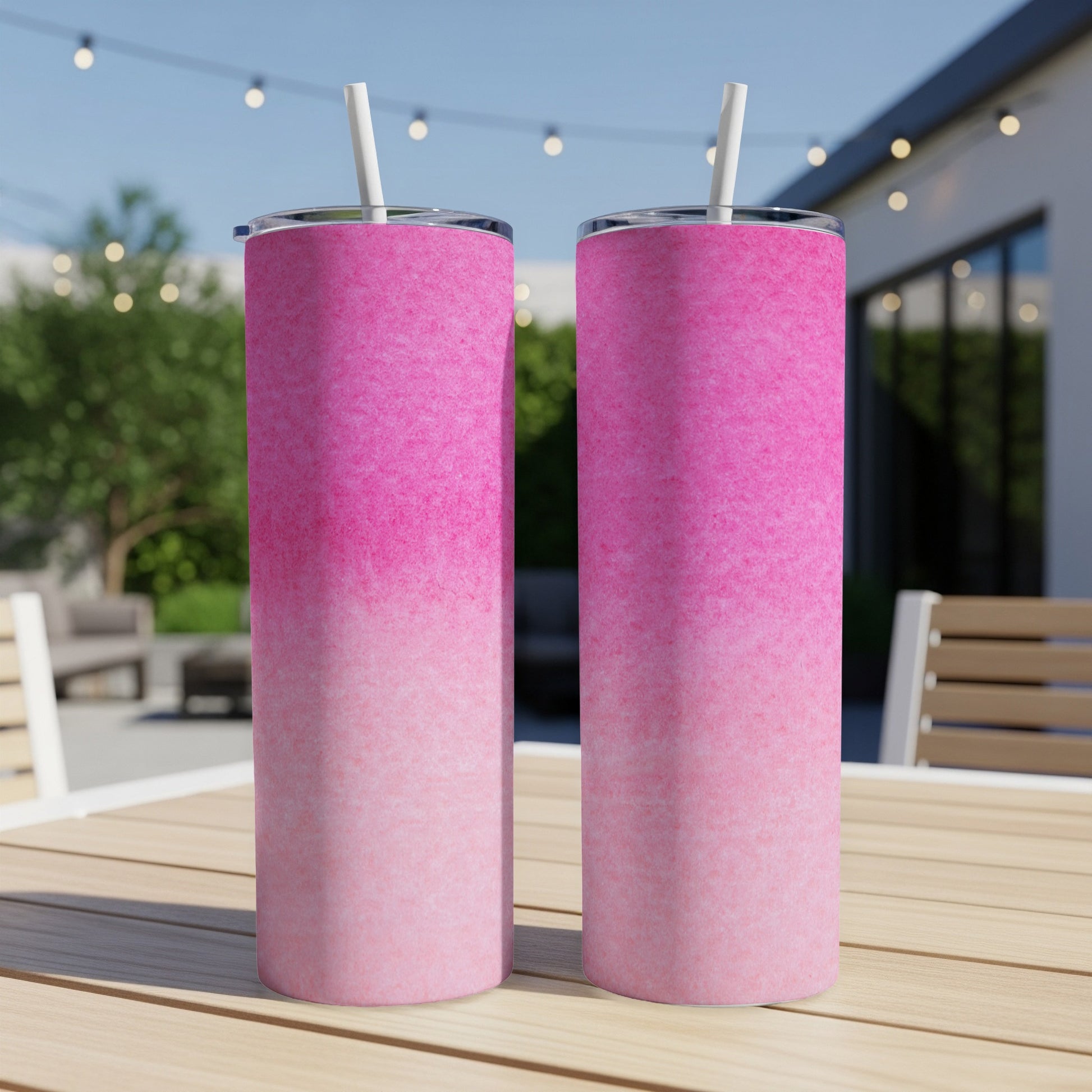 Two pink ombre tumblers with straws on a wooden table.