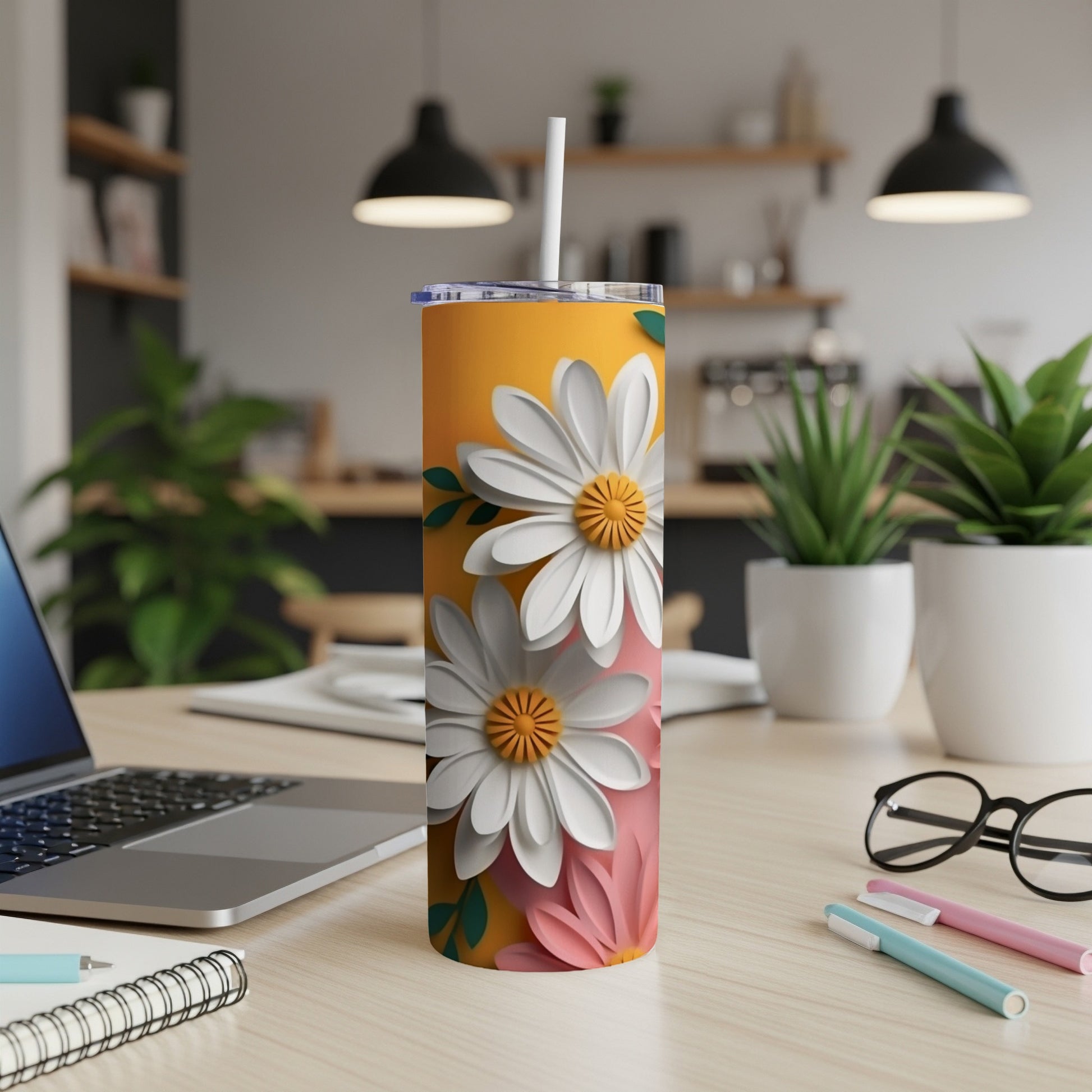 Orange tumbler with white and pink daisies, straw, laptop, and pens.