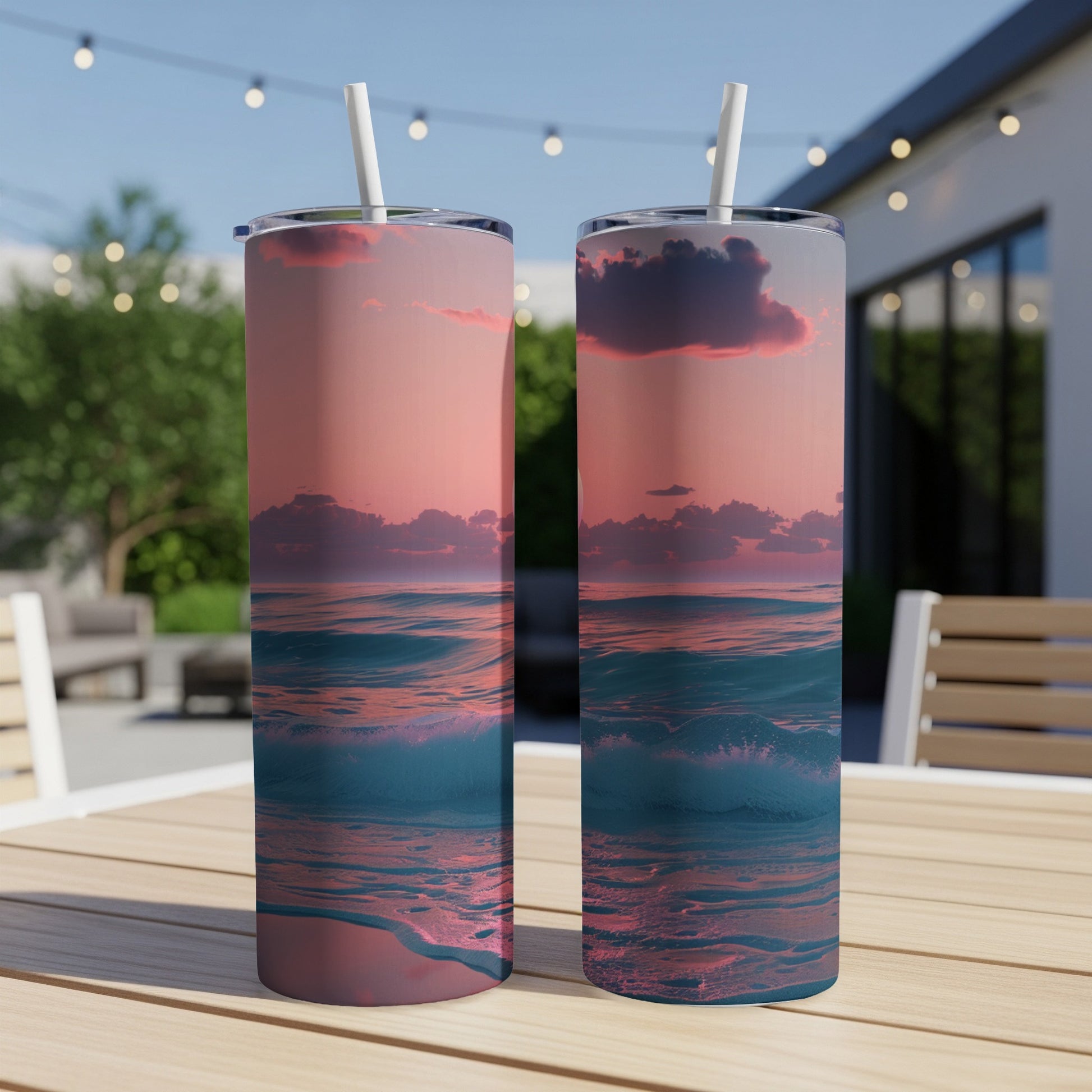 Two tall tumblers with a sunset ocean wave design on a wooden table.