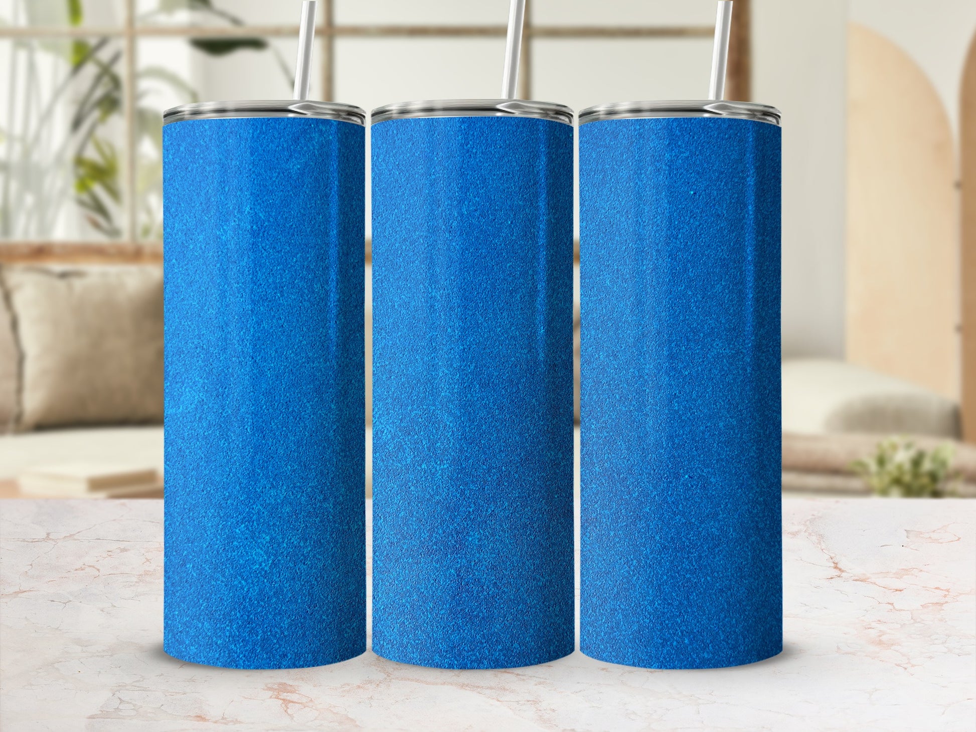 Three sparkly blue tumblers with straws on a marble surface.