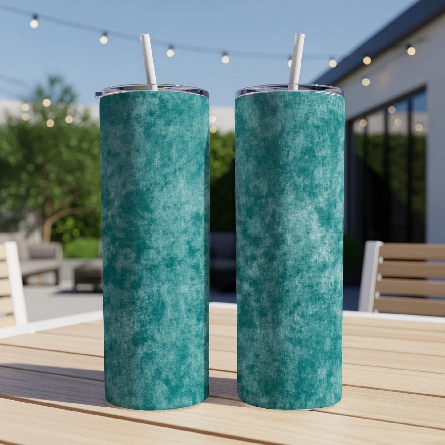 Two teal tumblers with white straws stand on a wooden table outdoors.