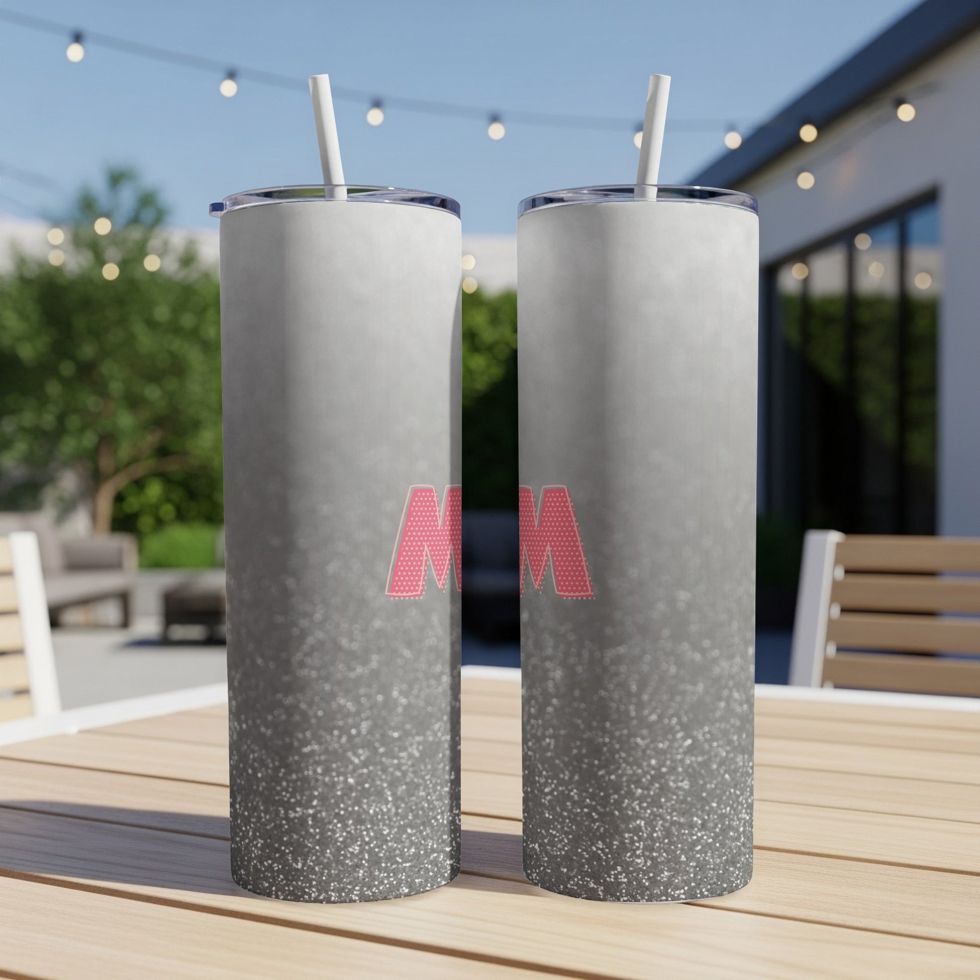 Two glitter-covered tumblers with "MOM" in pink lettering on a patio table.