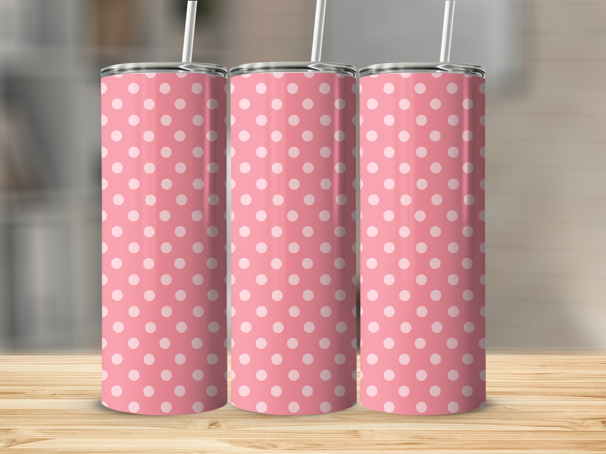 Three pink tumblers with white polka dots and straws on a wooden surface.