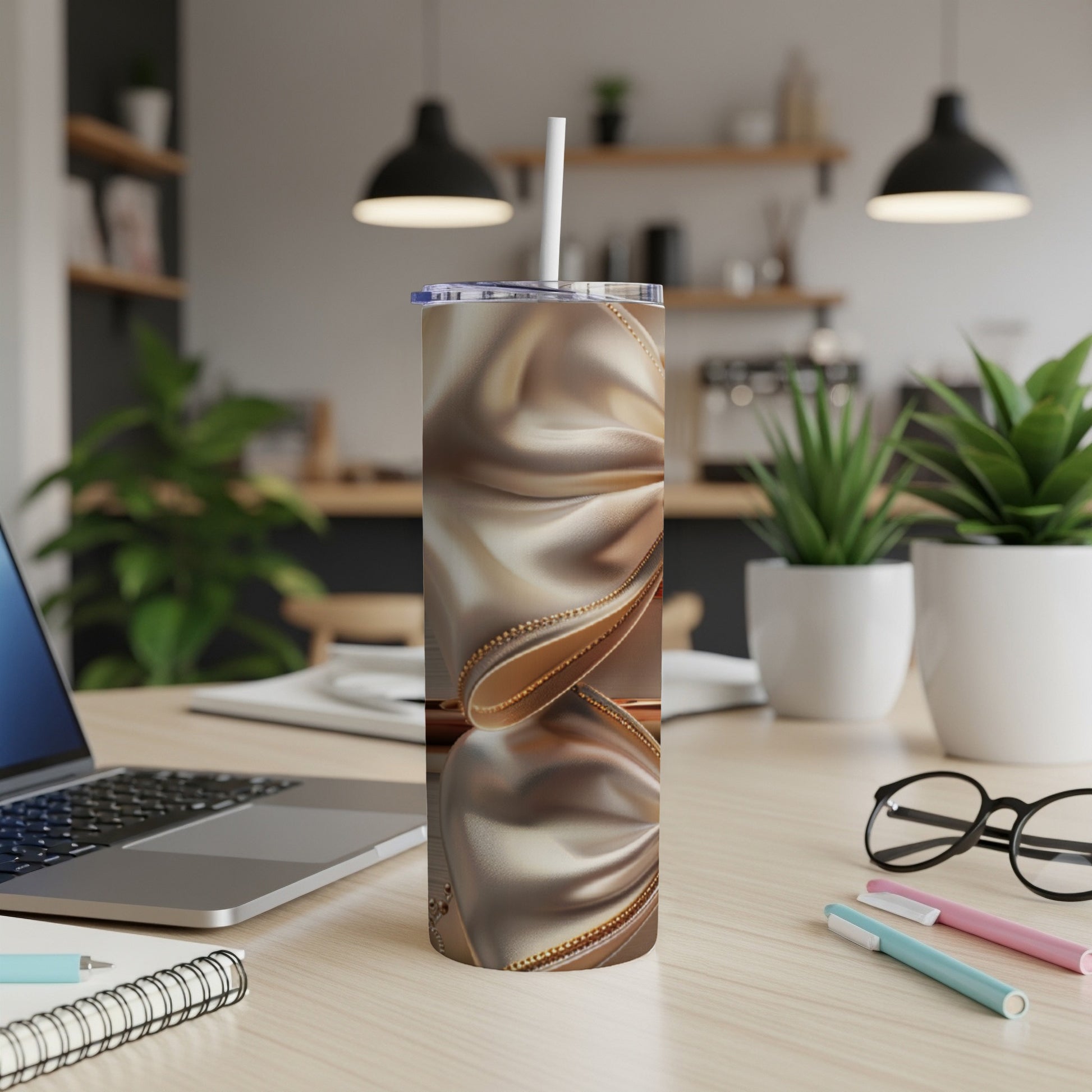 Satin-wrapped tumbler with gold trim and straw, on a desk.