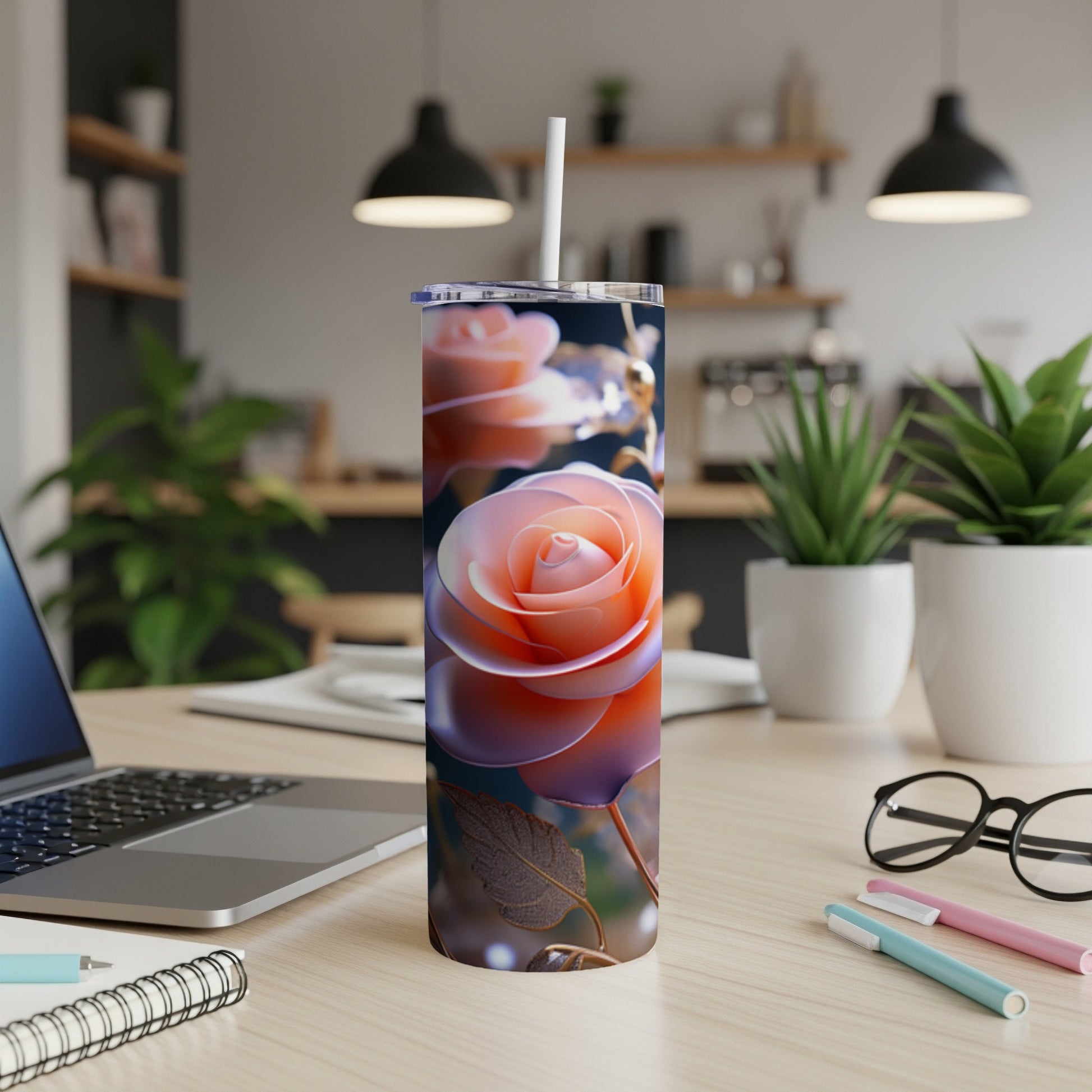 Pink rose on a tumbler next to a laptop and pens on a desk.