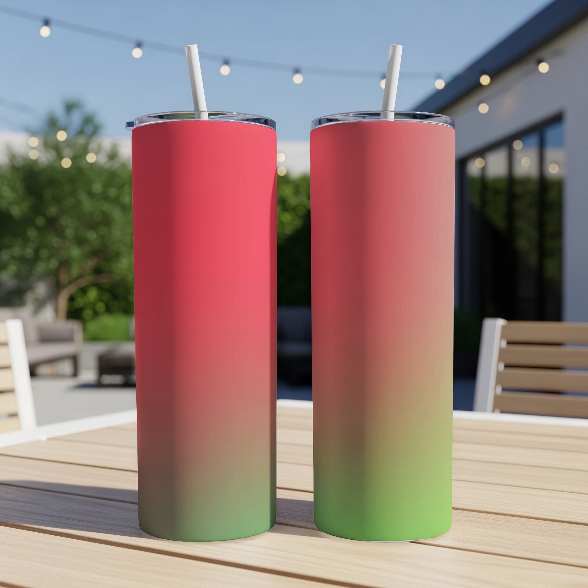 Two tall, slim gradient tumblers, red to green, with white straws on a wooden table.