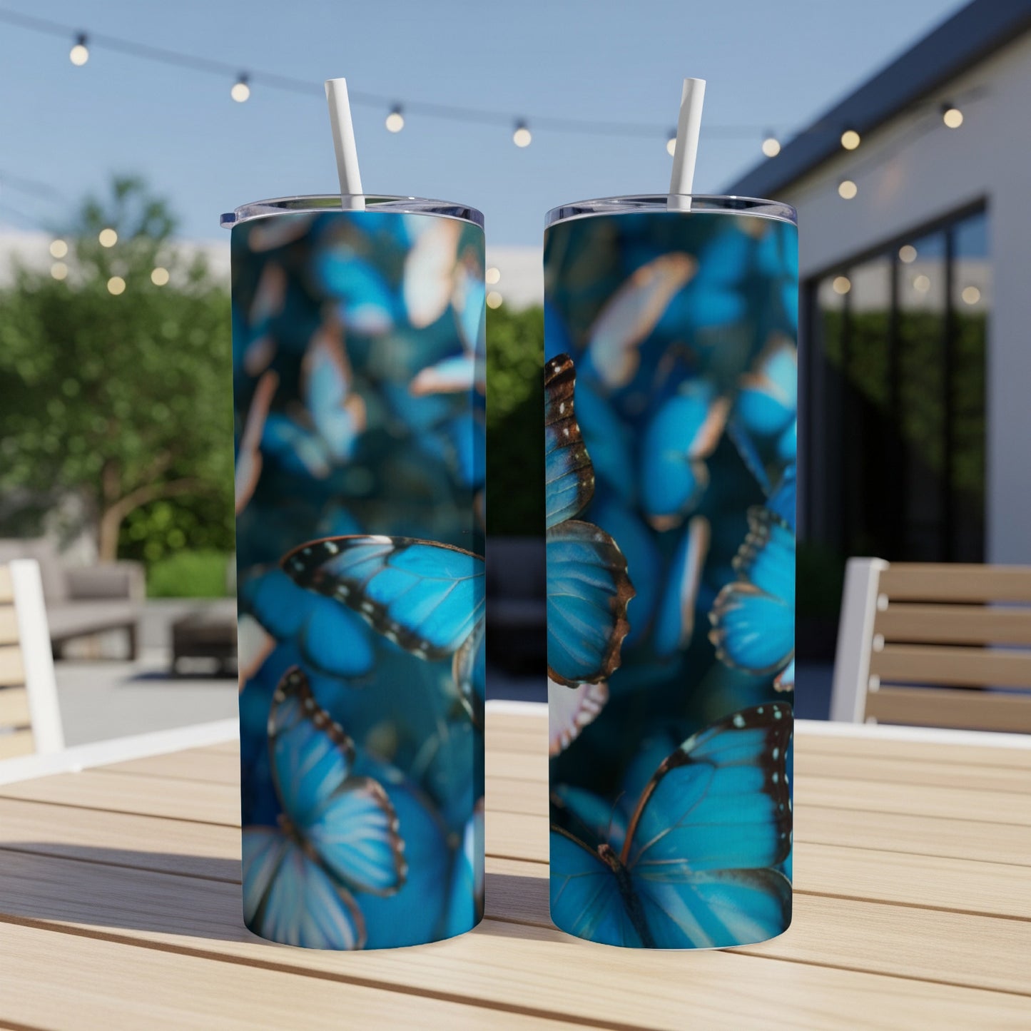 Two tall tumblers with a vibrant blue butterfly pattern displayed outdoors.