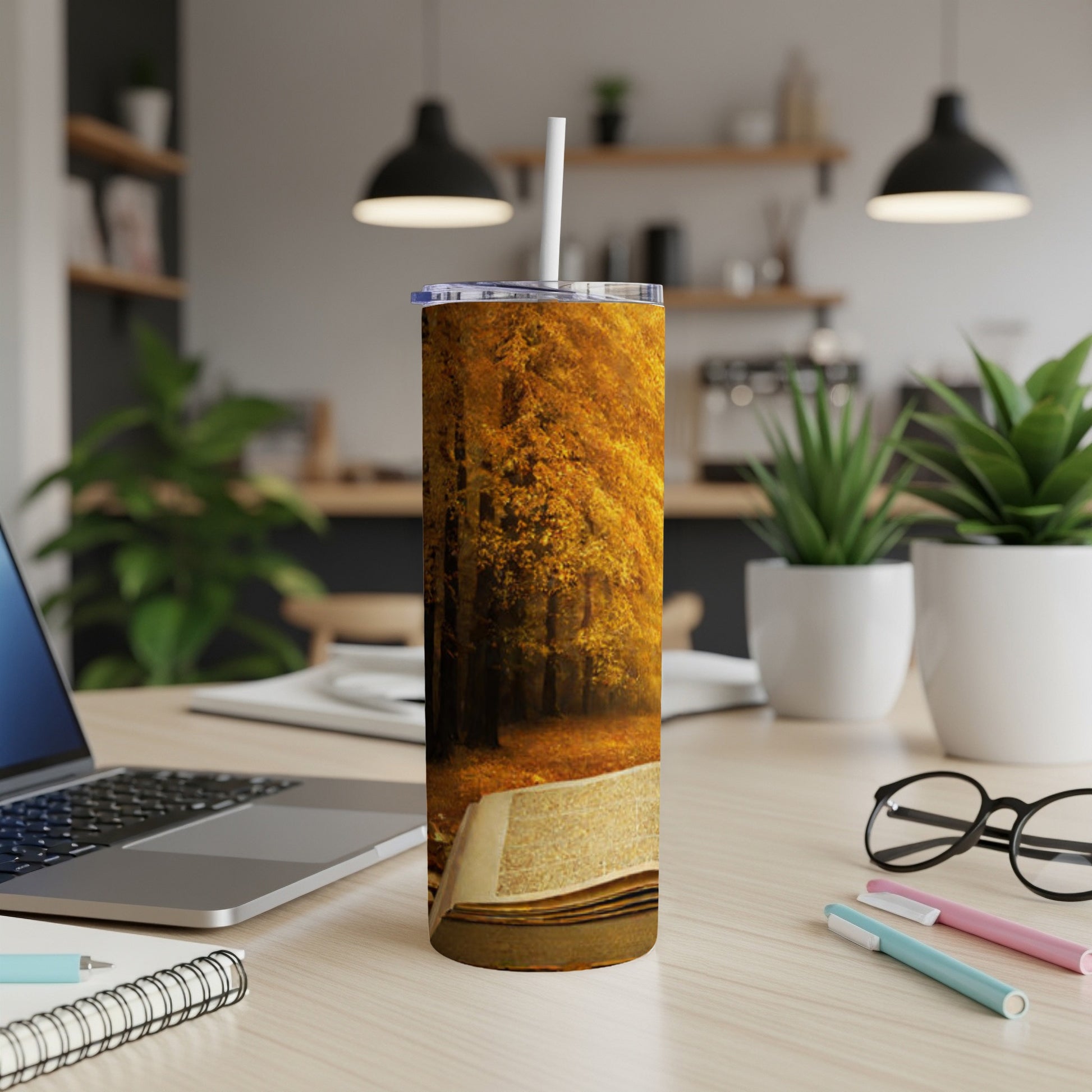 Tumbler with autumn forest scene and open book on desk.