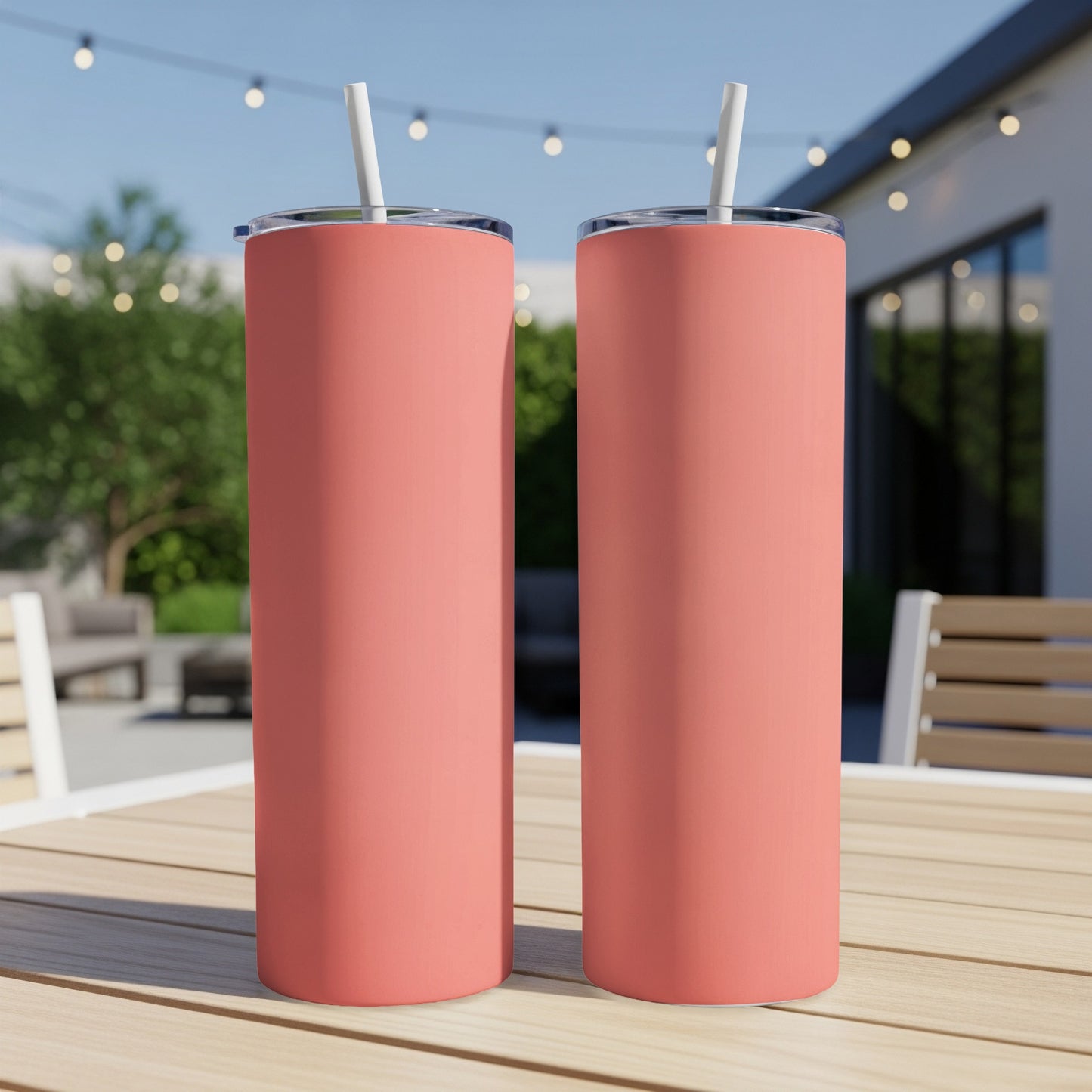 Two coral colored tumblers with white straws on a wooden table.