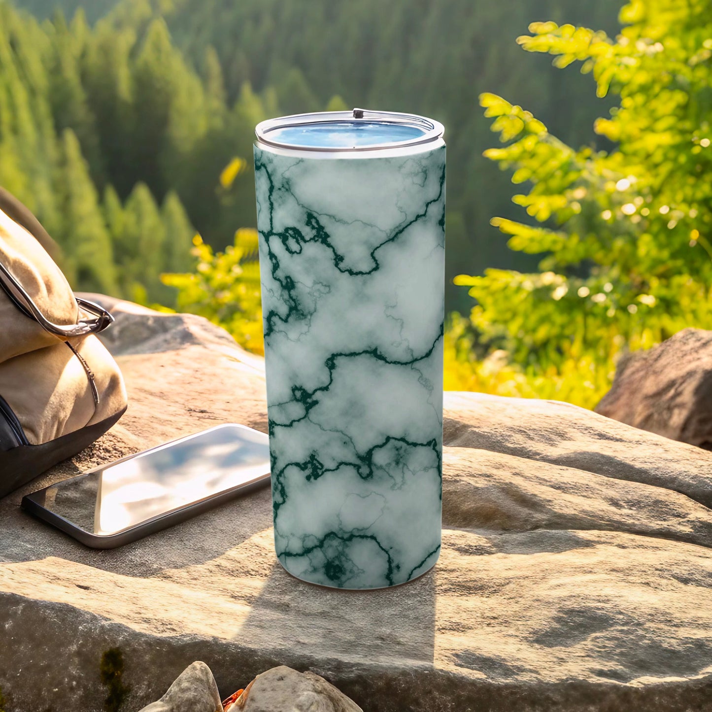 Green marble patterned tumbler with a smartphone and bag on rocks.