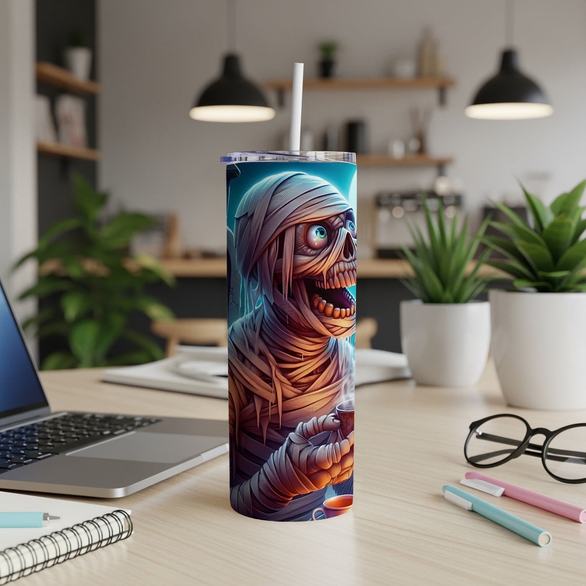 Tumbler with a mummy character holding a coffee cup, set on a desk.
