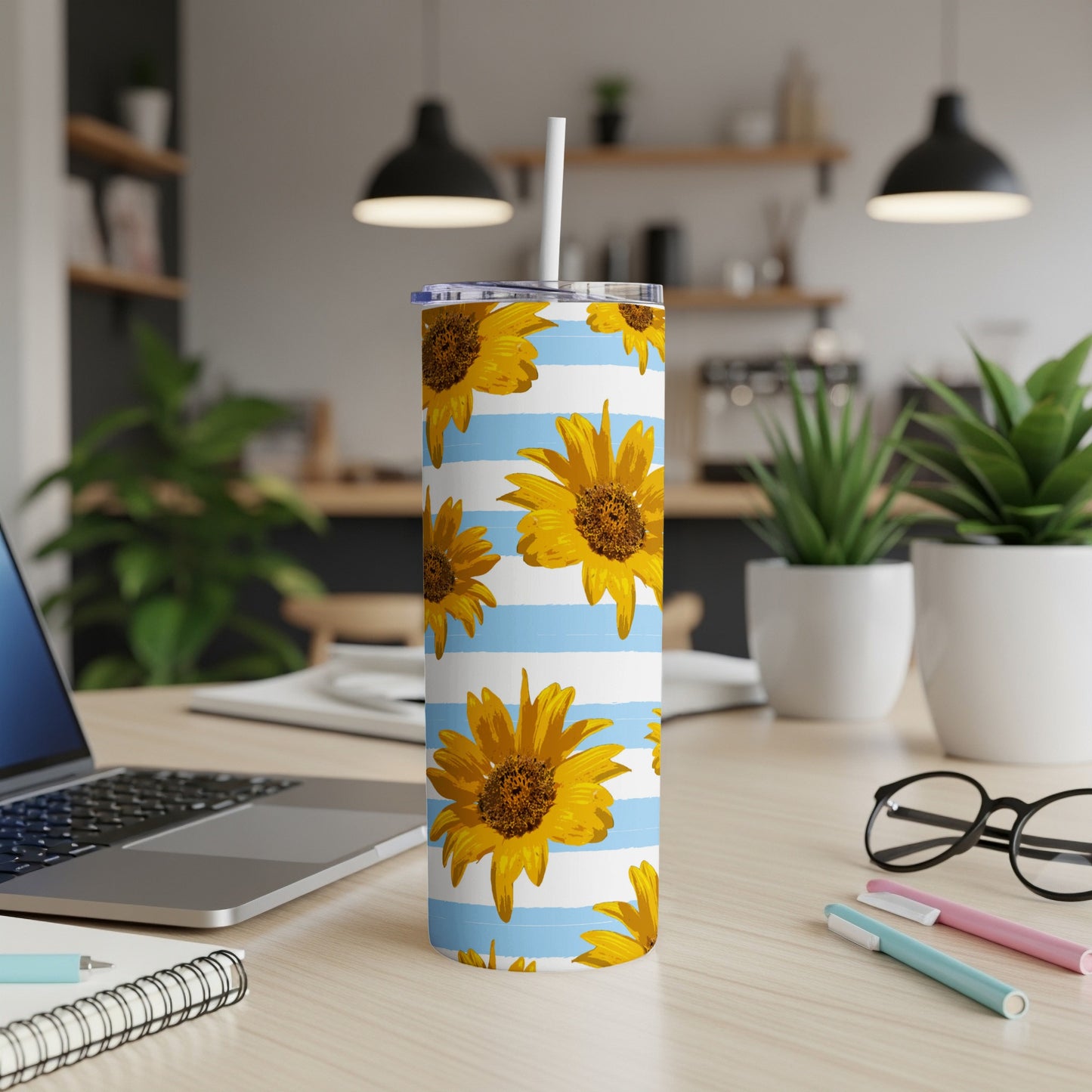 Sunflower tumbler with blue and white stripes on a desk with a laptop and plants.