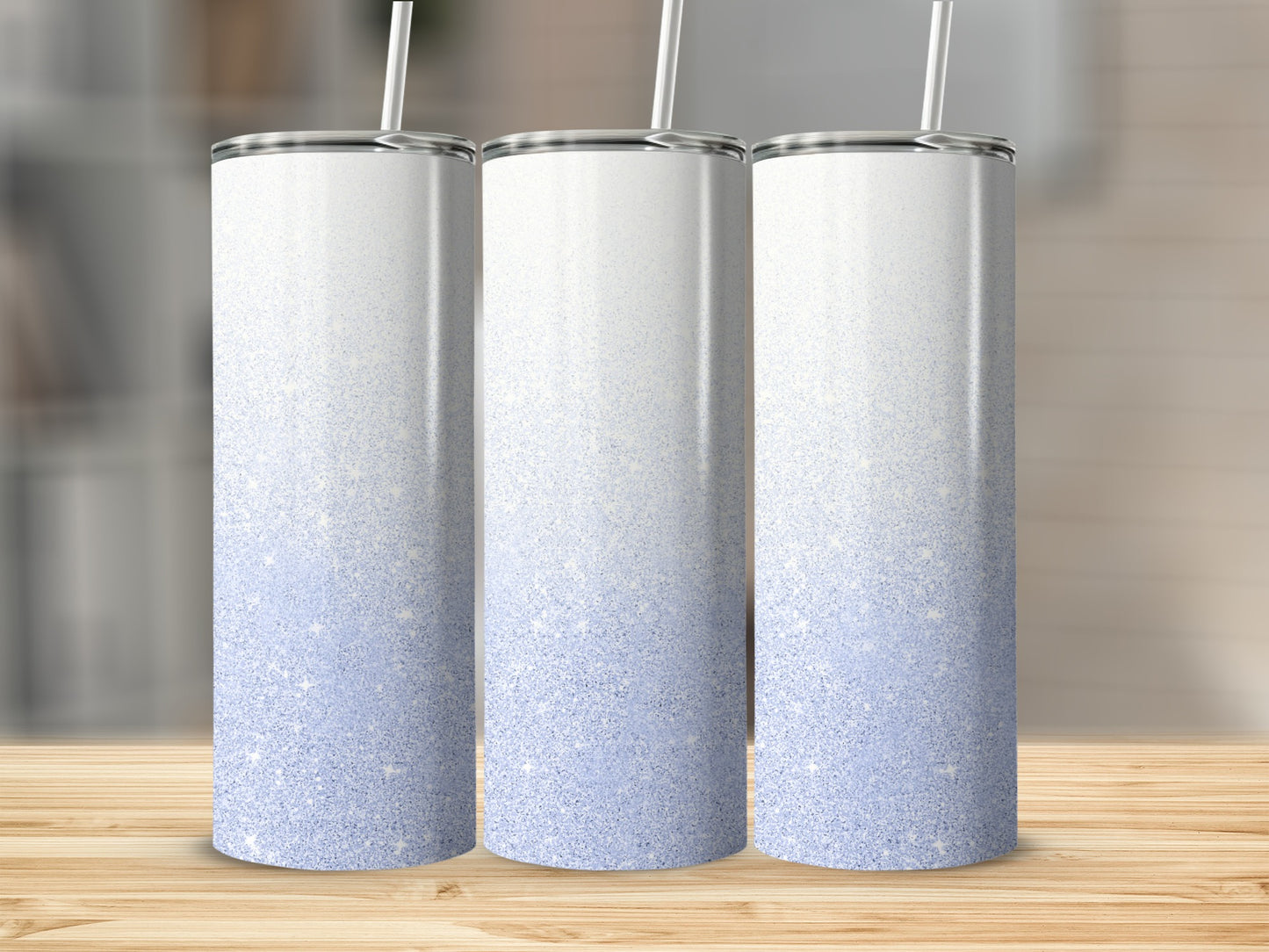 Three glittery white to light blue gradient tumblers with straws on a wooden surface.