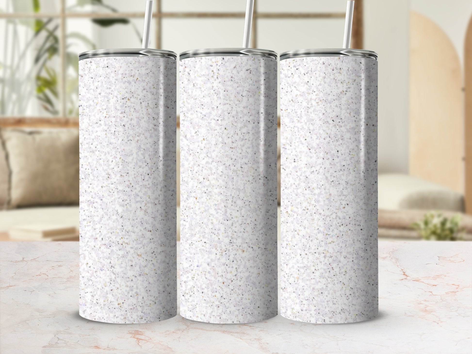 Three speckled glitter tumblers with straws on a marble surface.