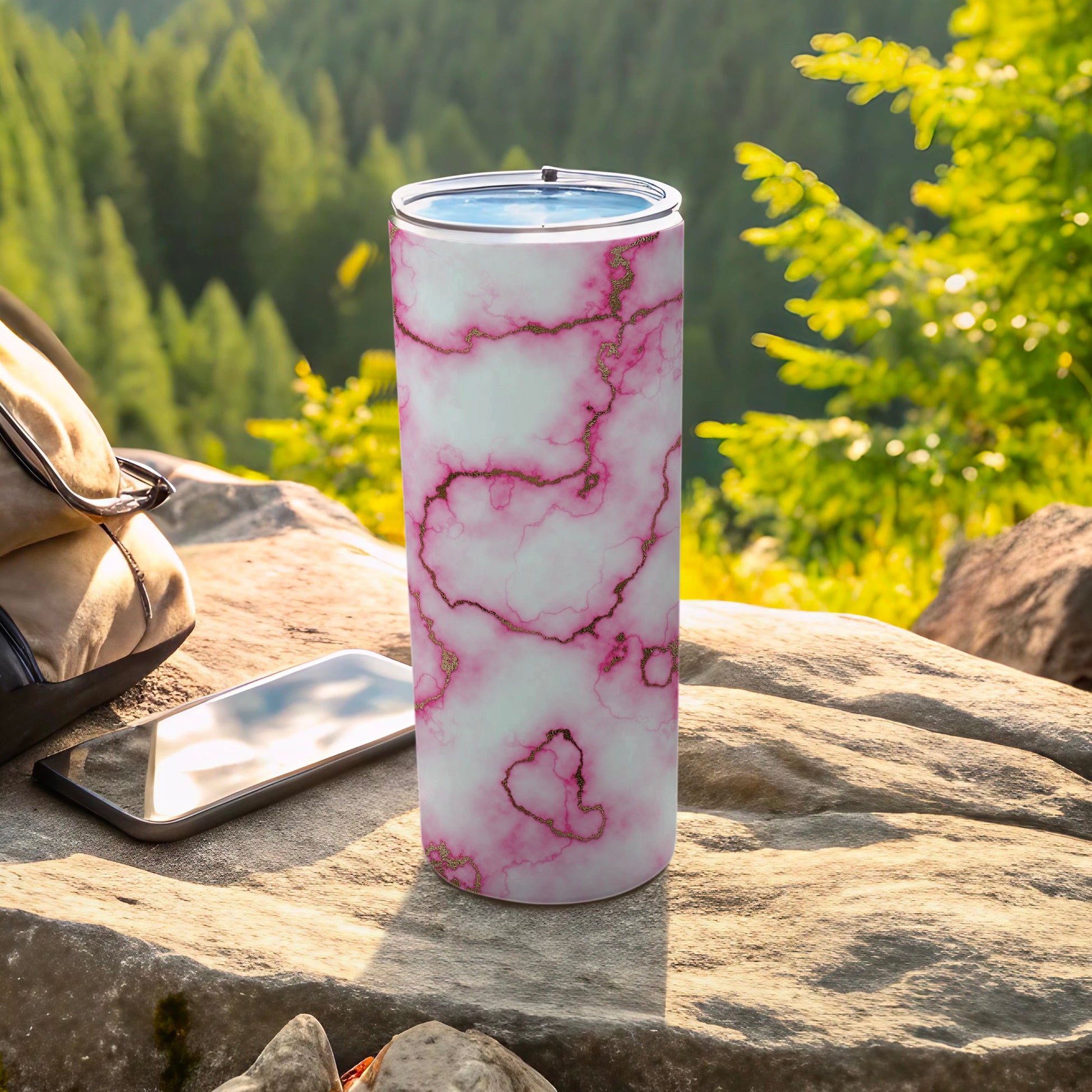 White marble tumbler with pink gold veins on a rock with phone and bag.