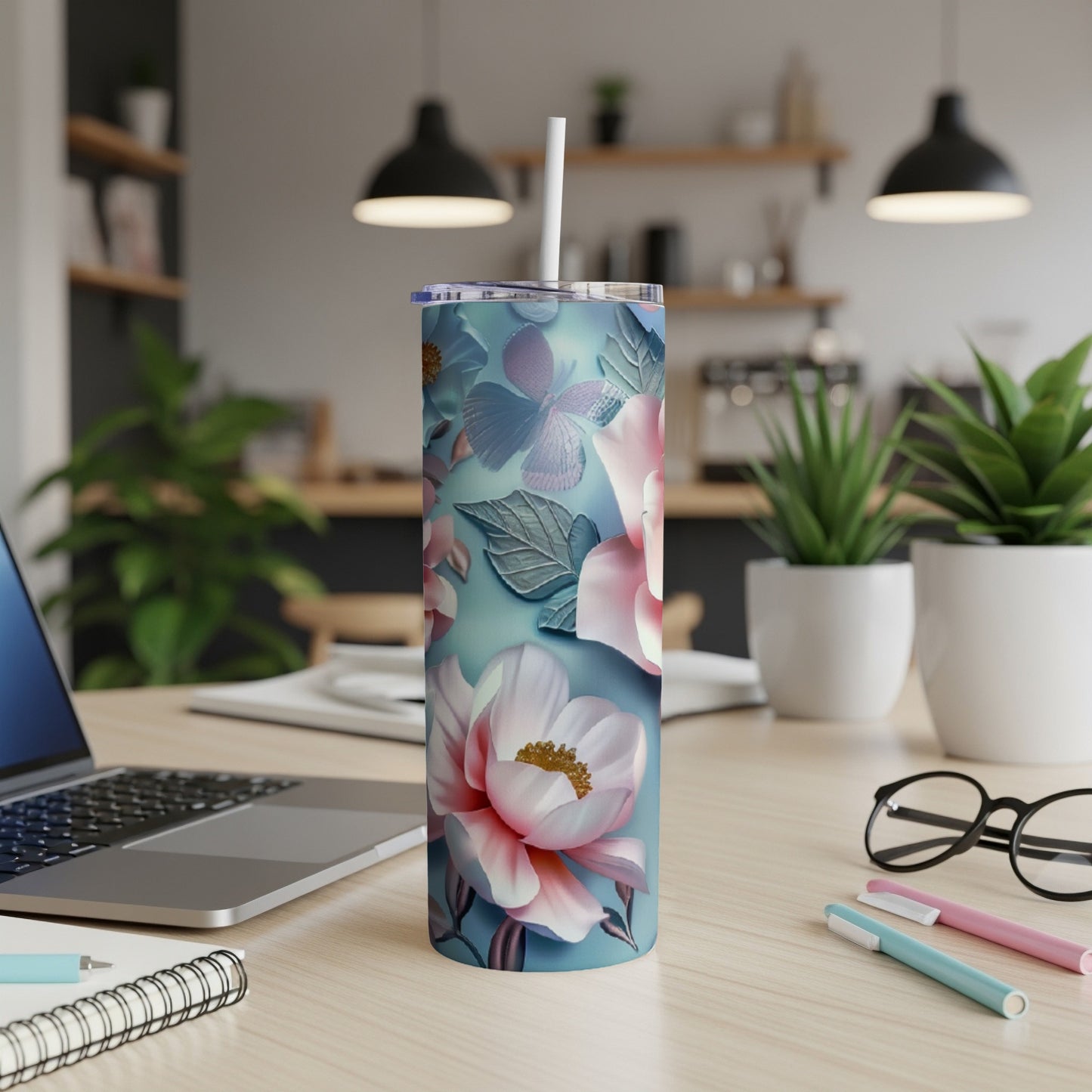 Tall tumbler with a floral design on a desk with a laptop and pens.