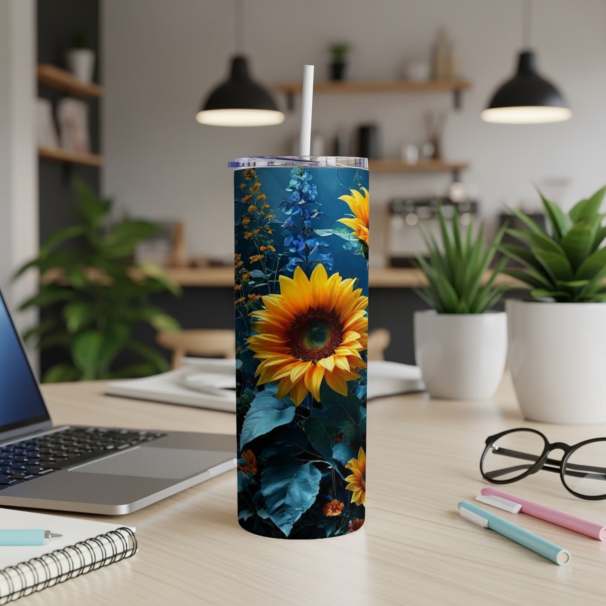 Tall tumbler with sunflowers and blue flowers on a desk.