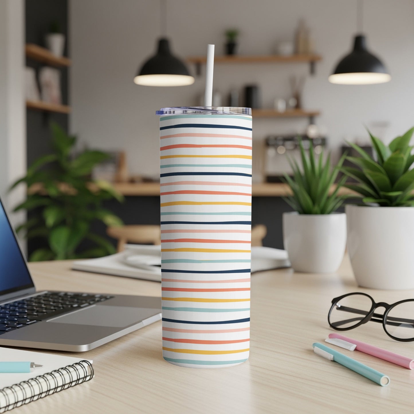 Multi-colored striped skinny tumbler with a straw on a desk.