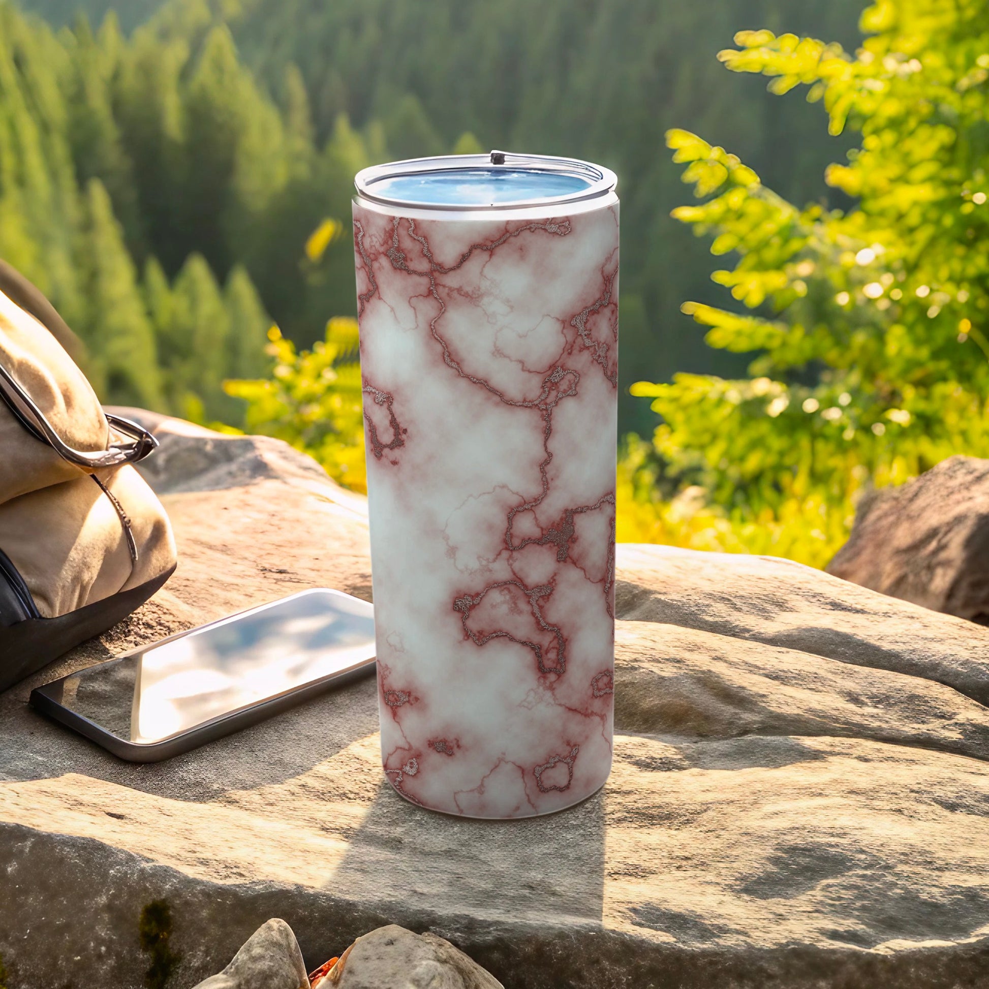 Marble-patterned tumbler with a phone and backpack on rocks.