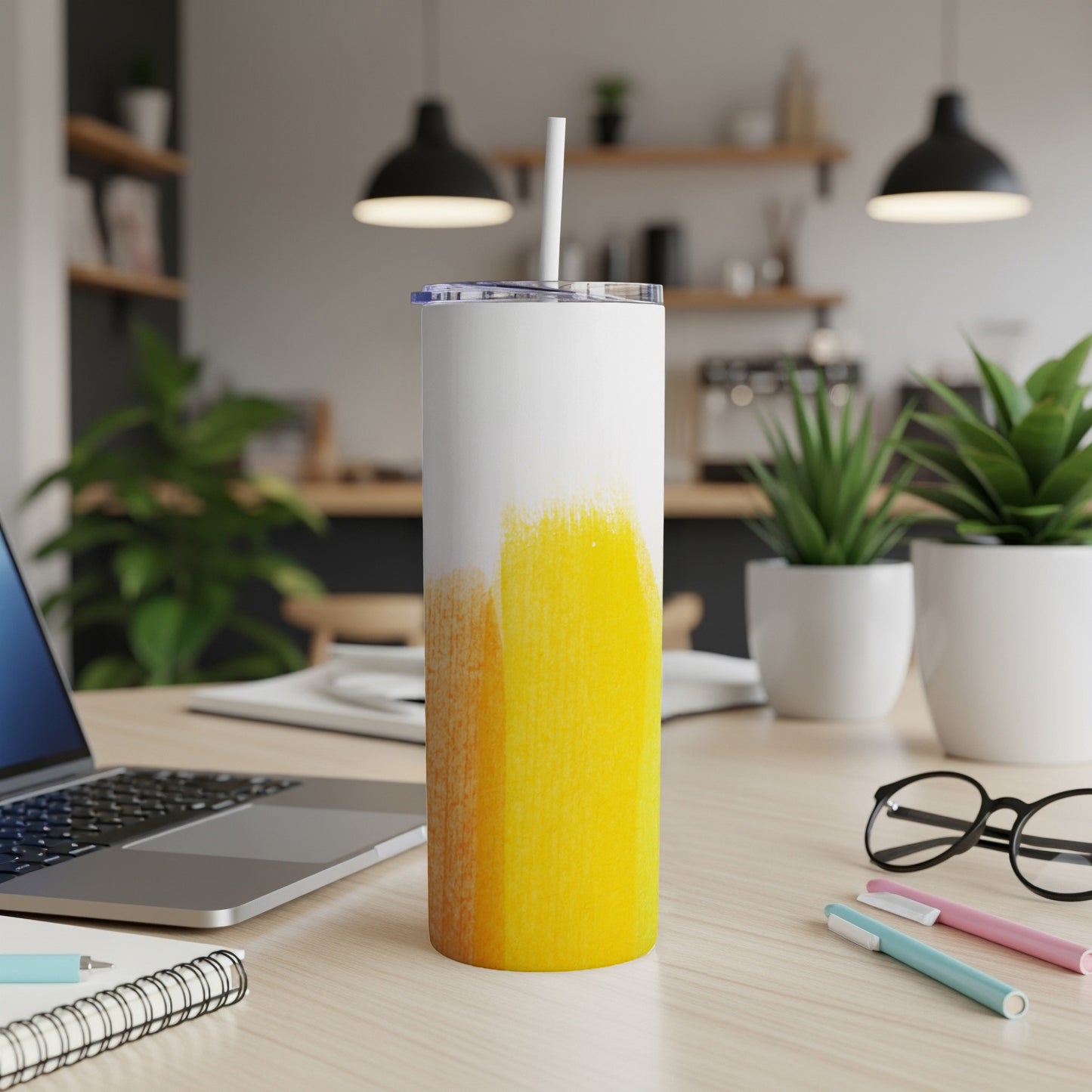 White and yellow abstract tumbler with straw on a desk with laptop.