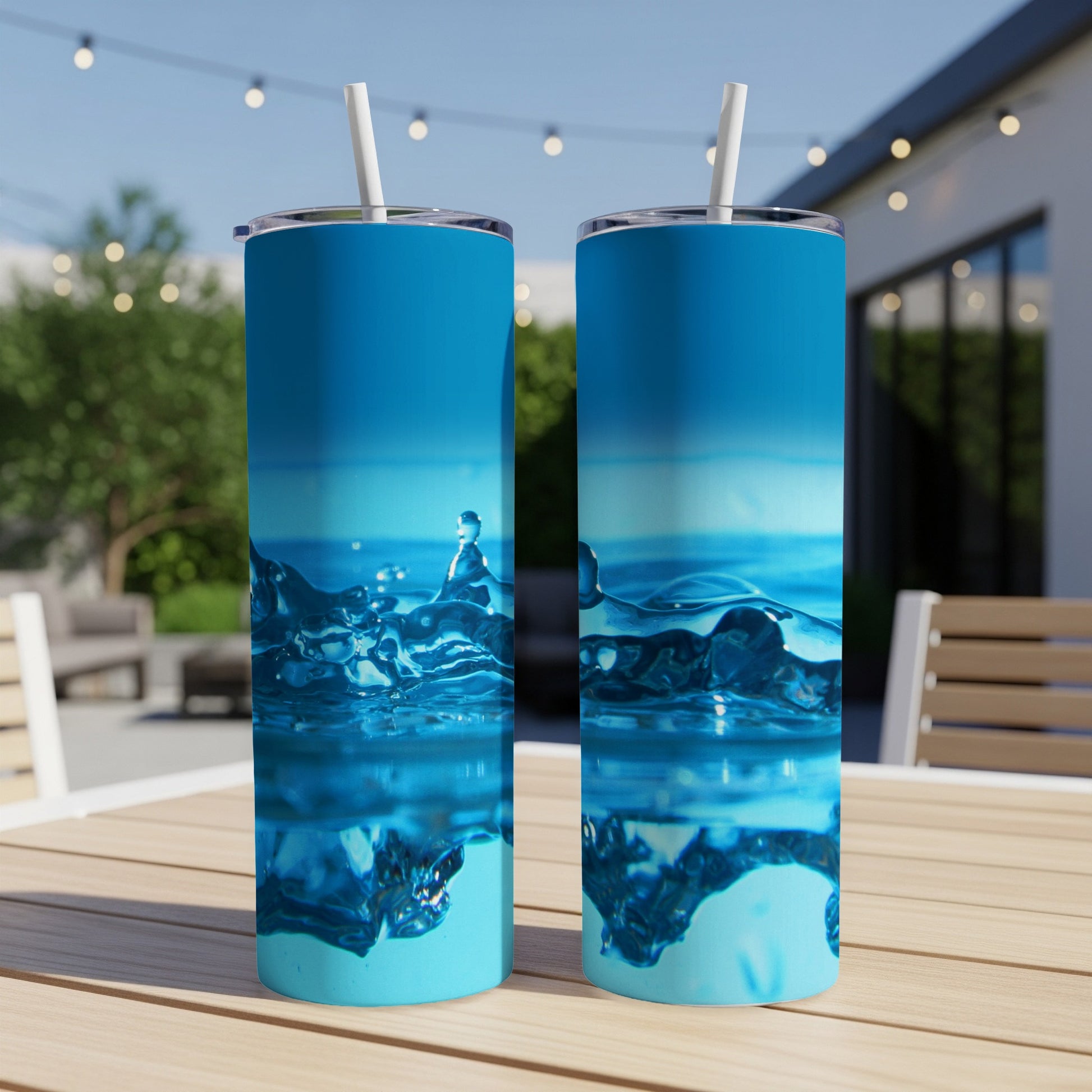 Two blue tumblers with water splash design sit on a wooden table outdoors.