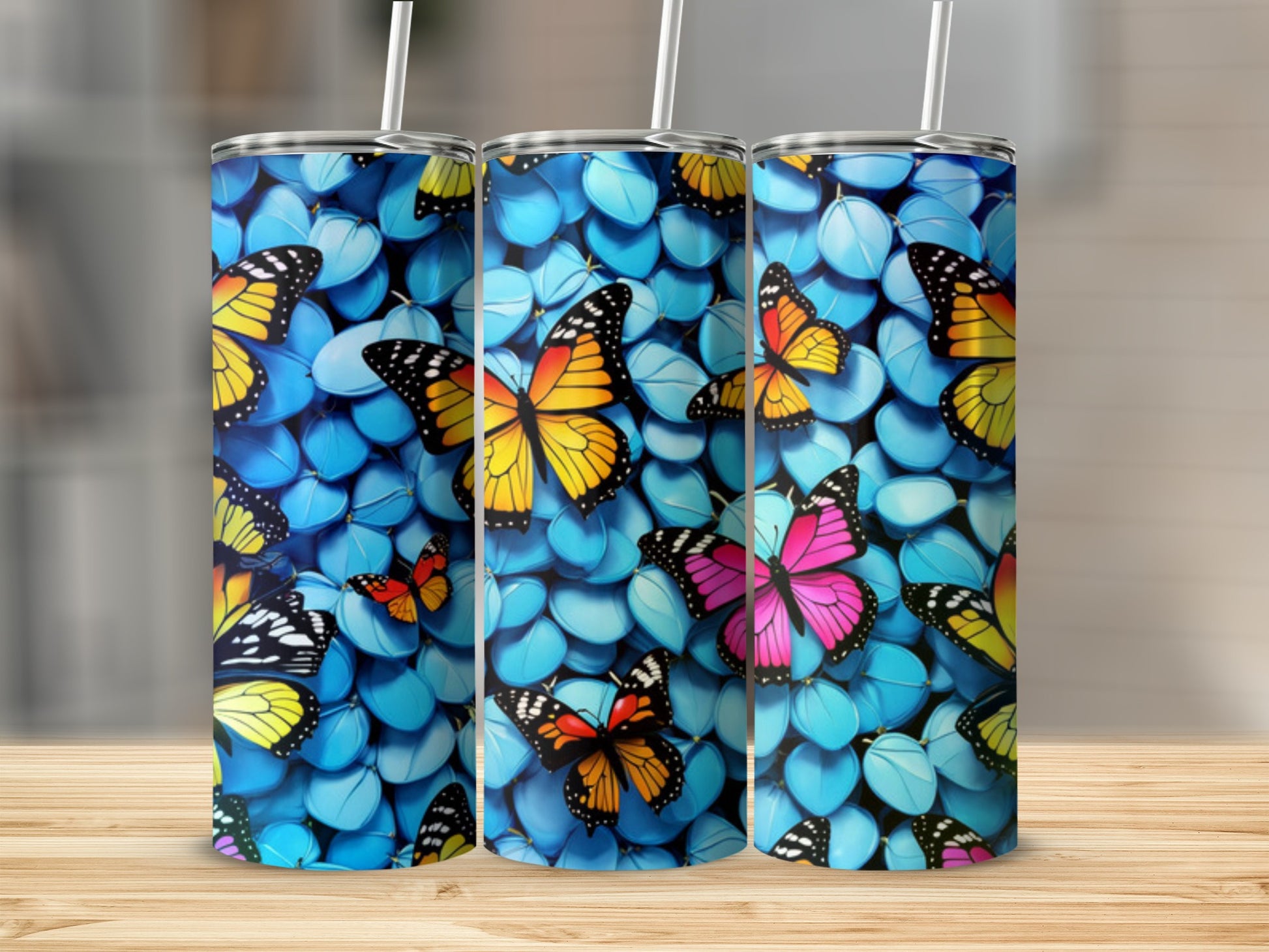 Three tumblers with vibrant butterfly designs on a blue, pebble-like background.