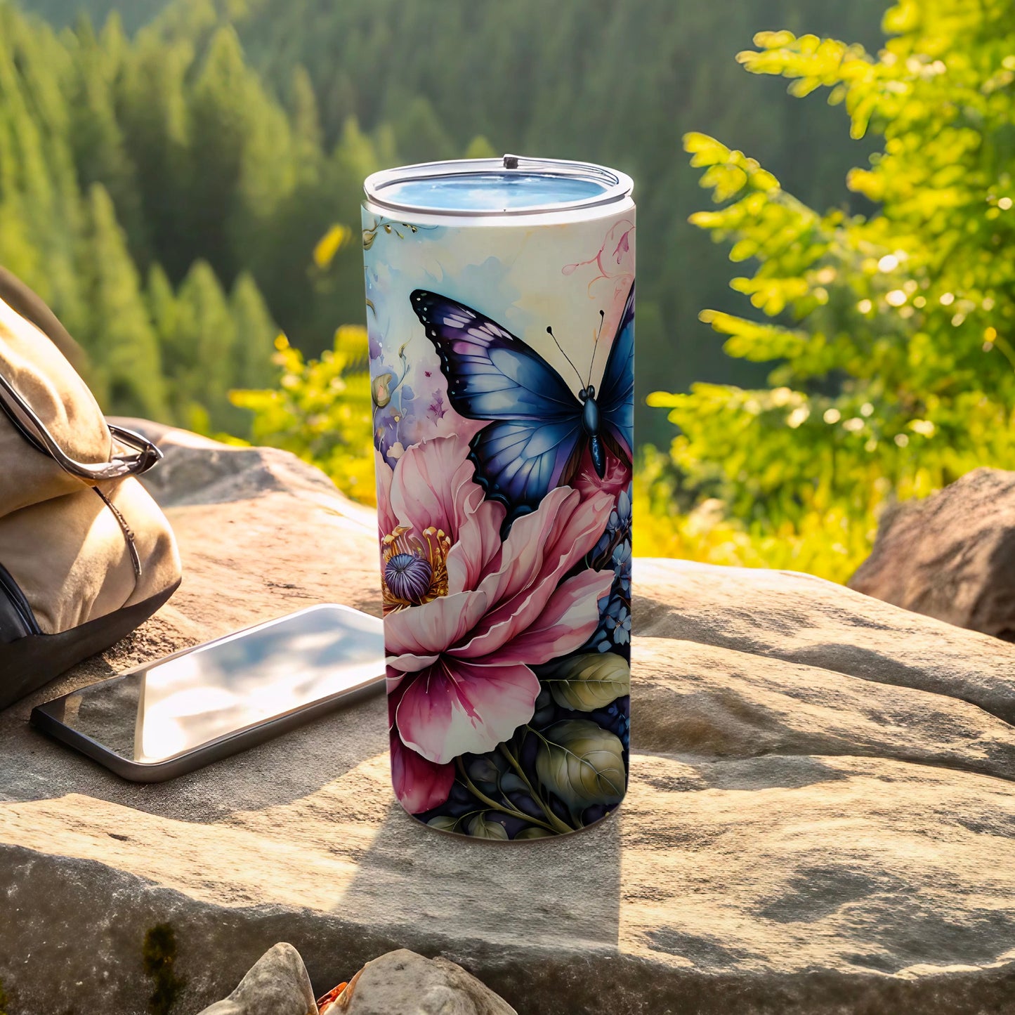 Tumbler with blue butterfly and pink floral design on outdoor rock surface.