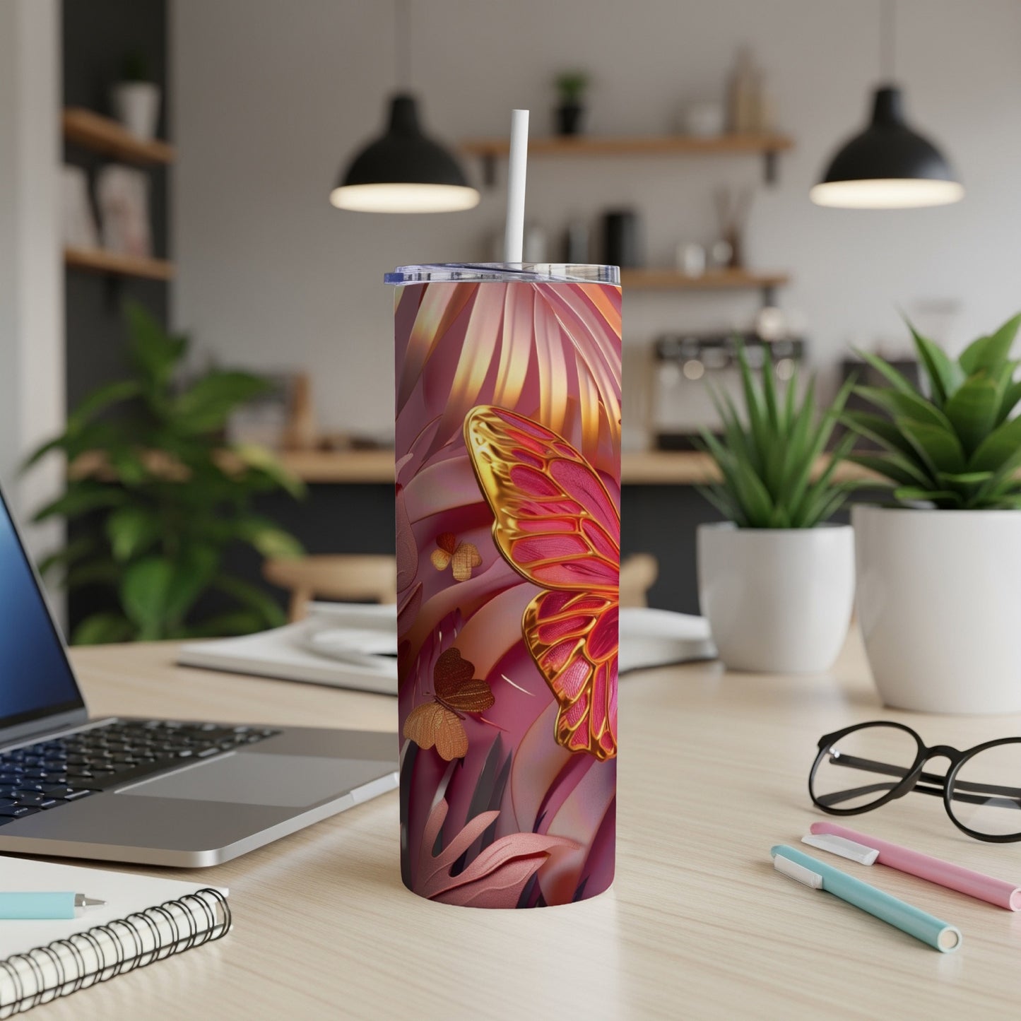 Pink and gold patterned tumbler with straw on a desk.