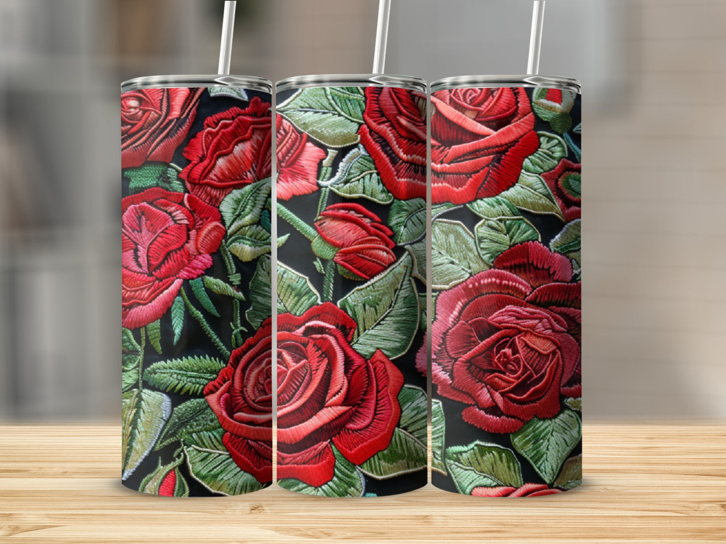 Three tumblers with a red rose embroidery pattern on a wooden surface.