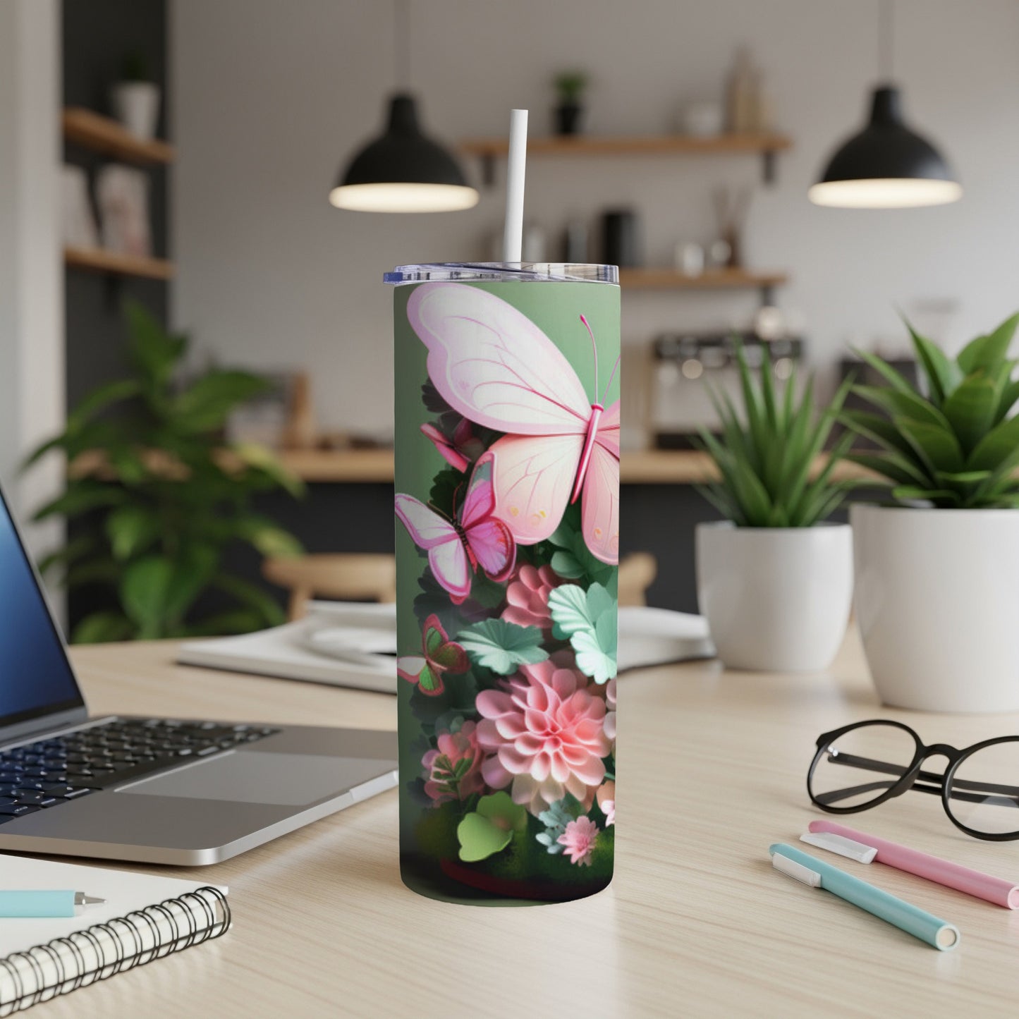 Green tumbler with butterflies and flowers, white straw, on desk with laptop.
