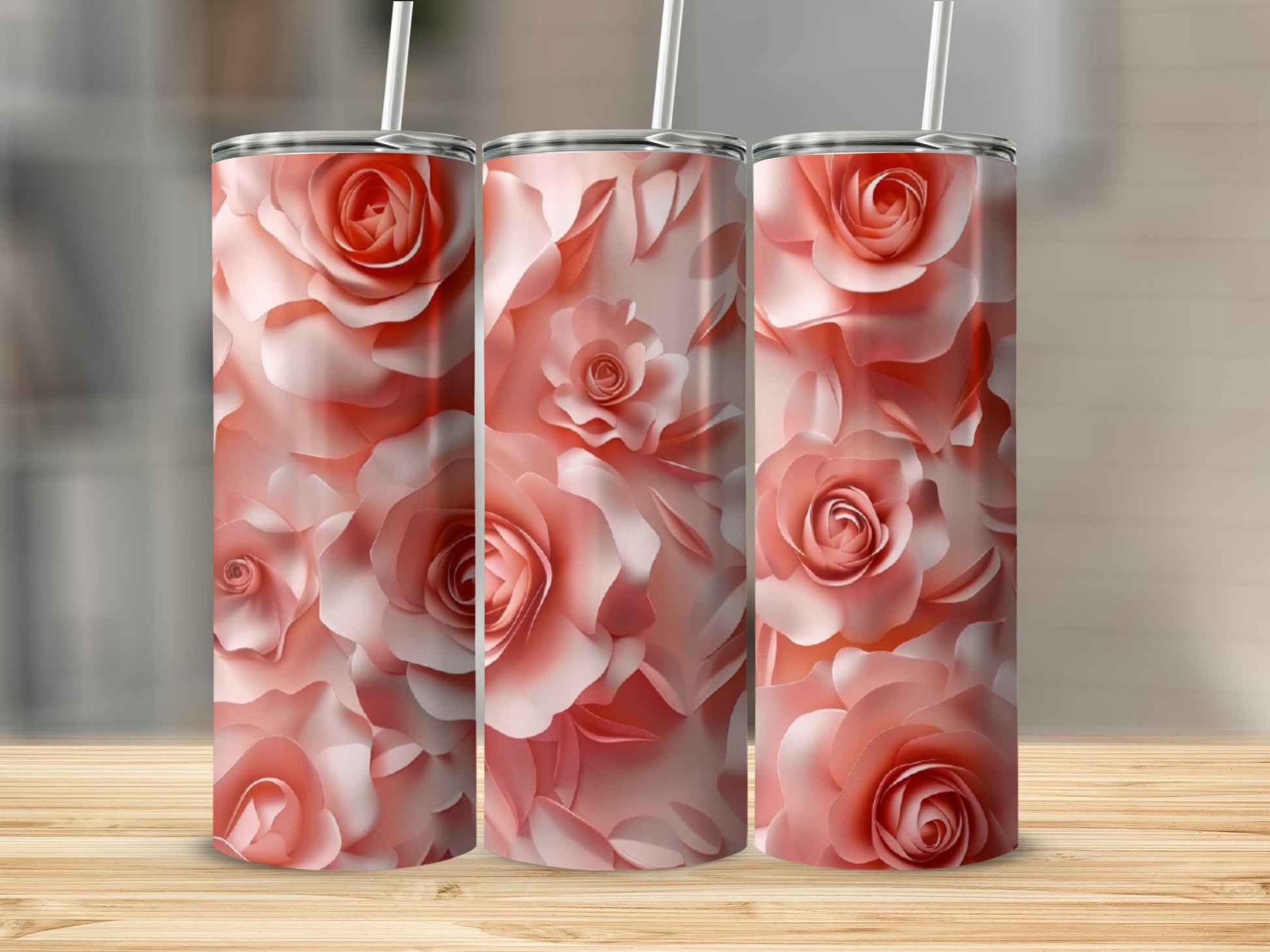 Three pink rose floral print tumblers with straws on a wooden surface.