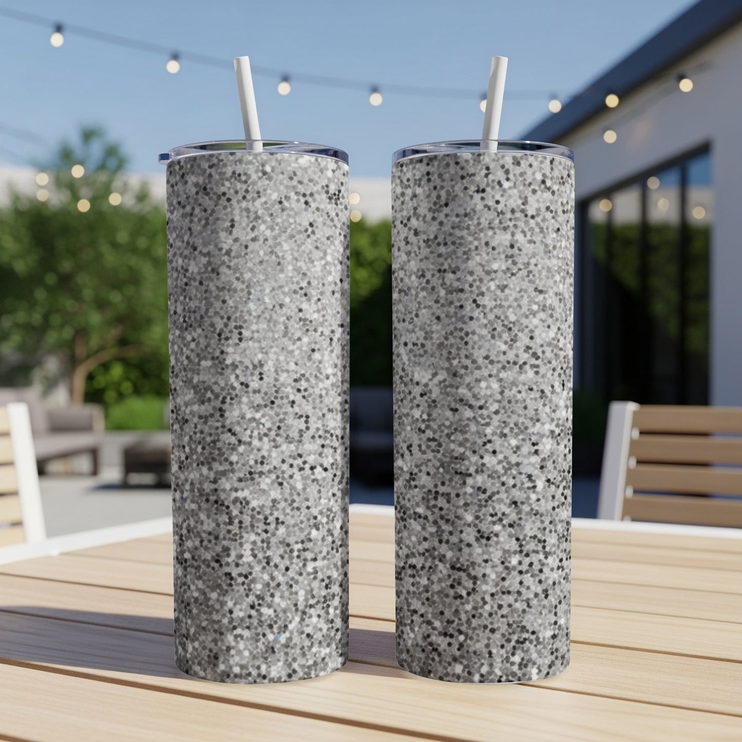 Two silver glitter tumblers with straws on a wooden table.