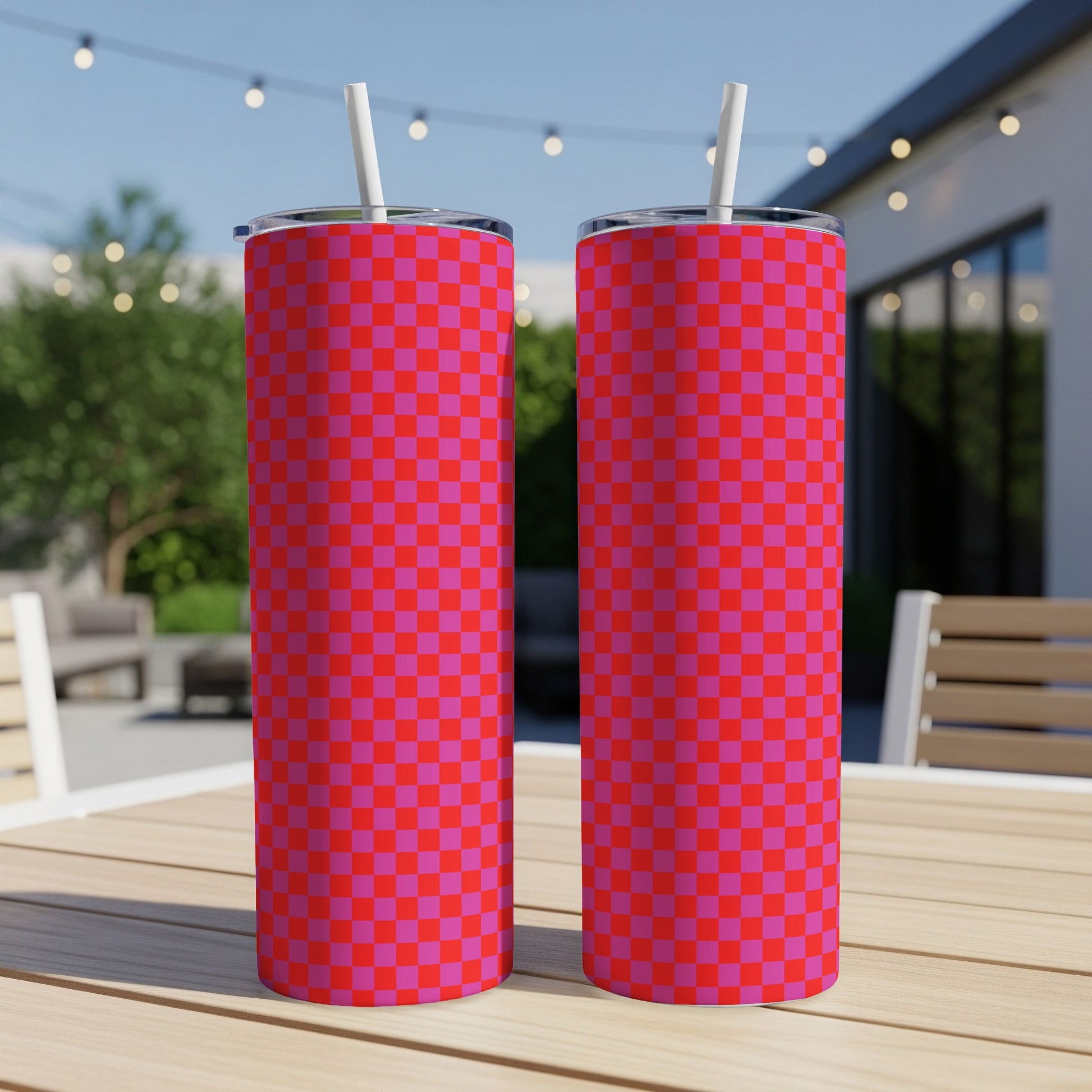 Two pink and red checkered tumblers with straws on a wooden table.