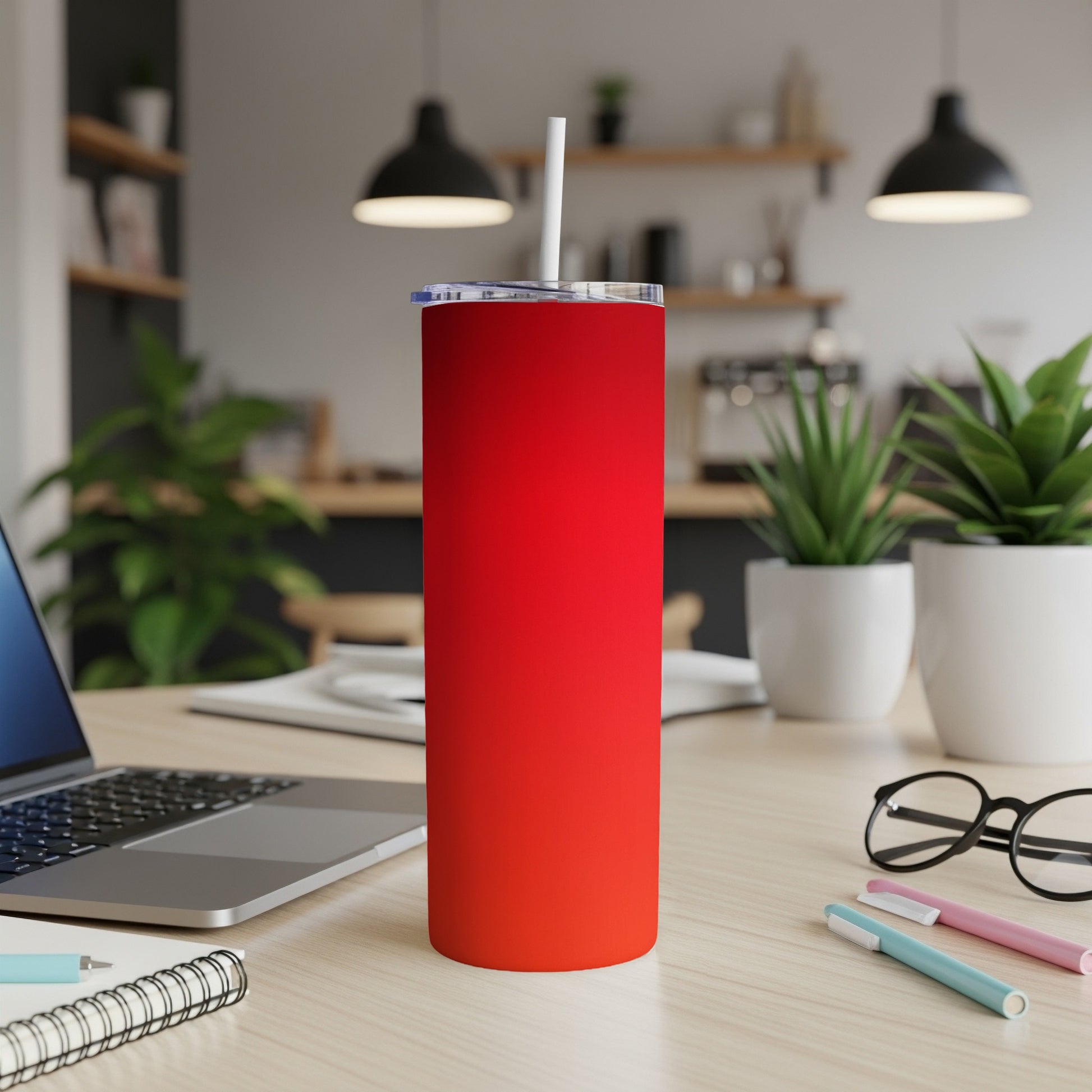 Red gradient tumbler with straw on a desk beside a laptop.