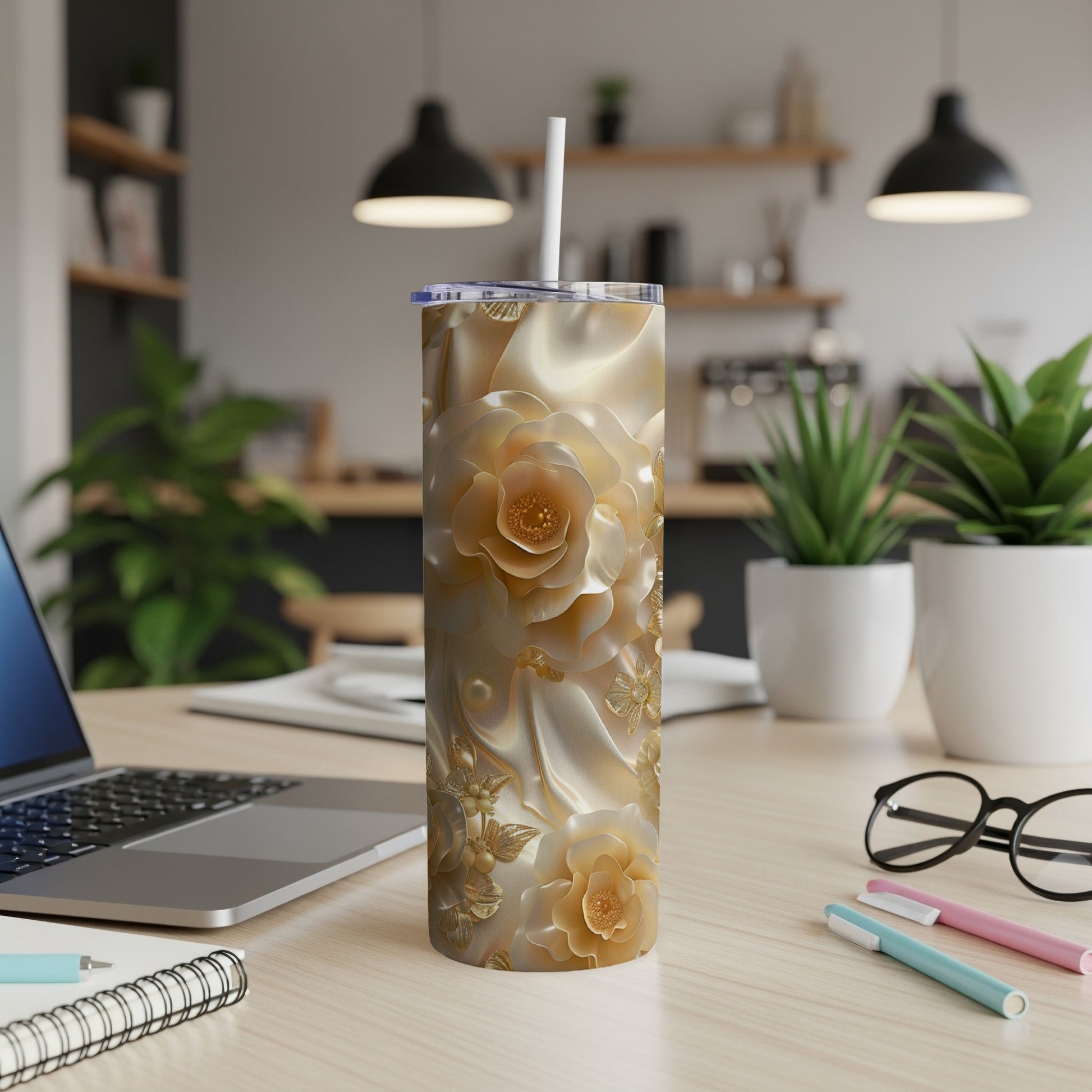 Gold floral pattern tumbler with straw on a desk next to a laptop.