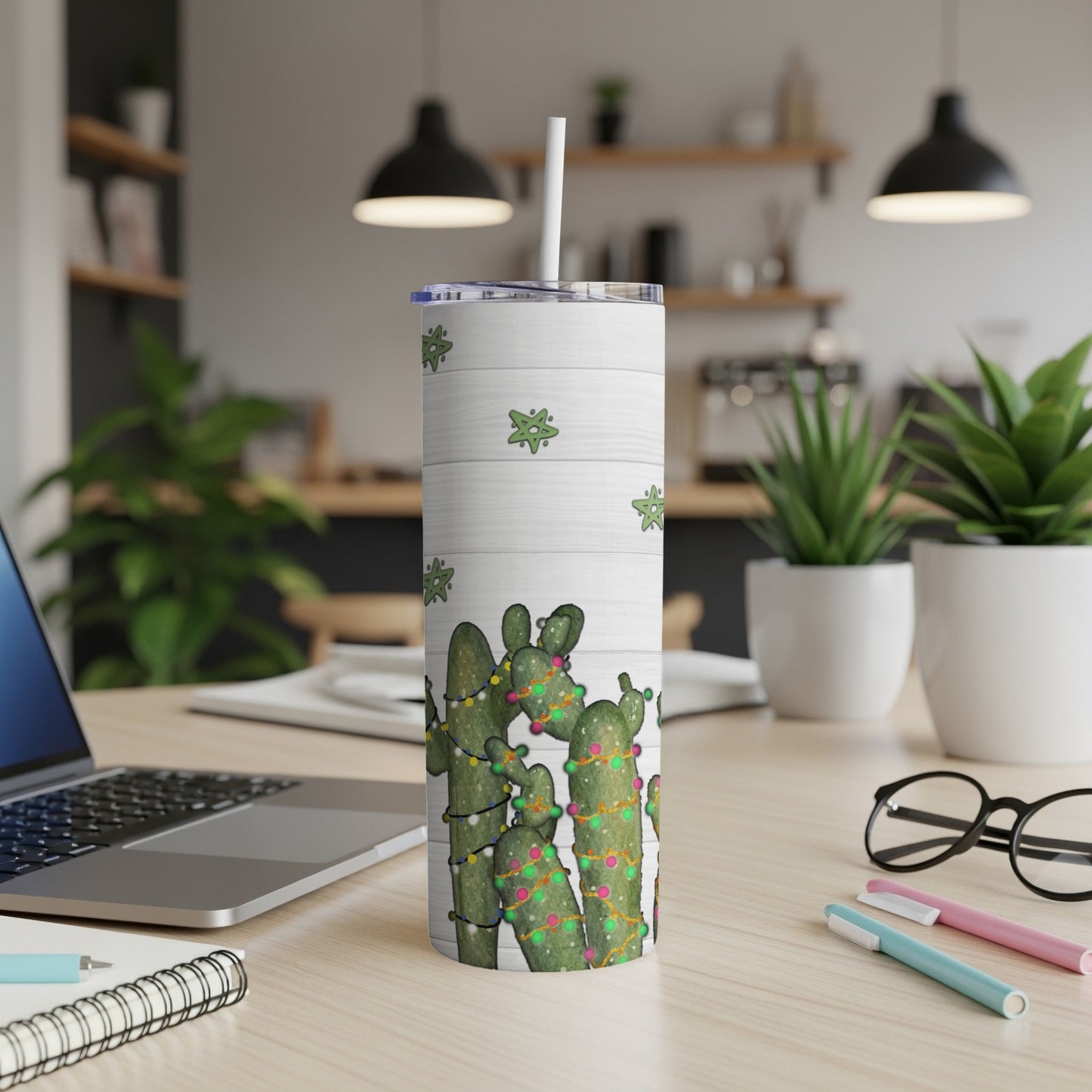 White tumbler with cactus design and green string lights on a desk.