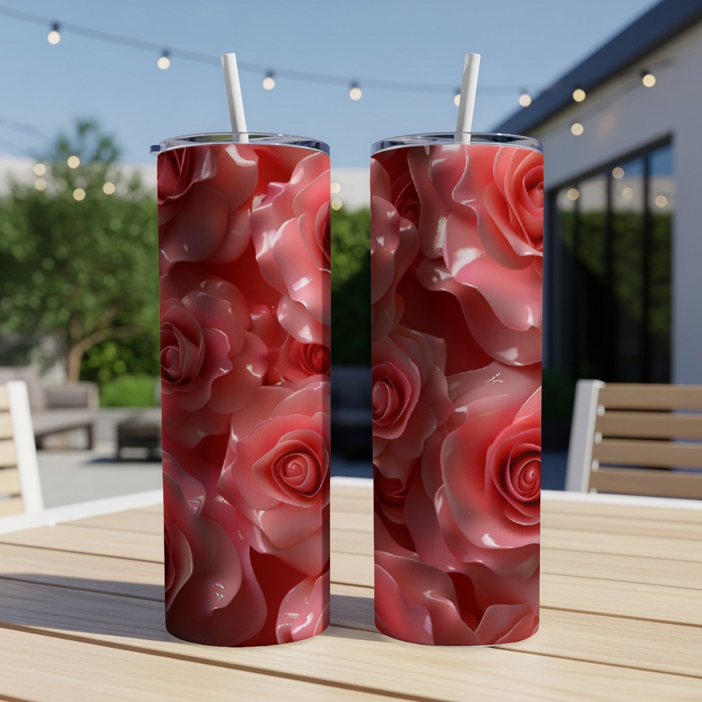 Two pink roses on a skinny tumbler with a straw on a table.