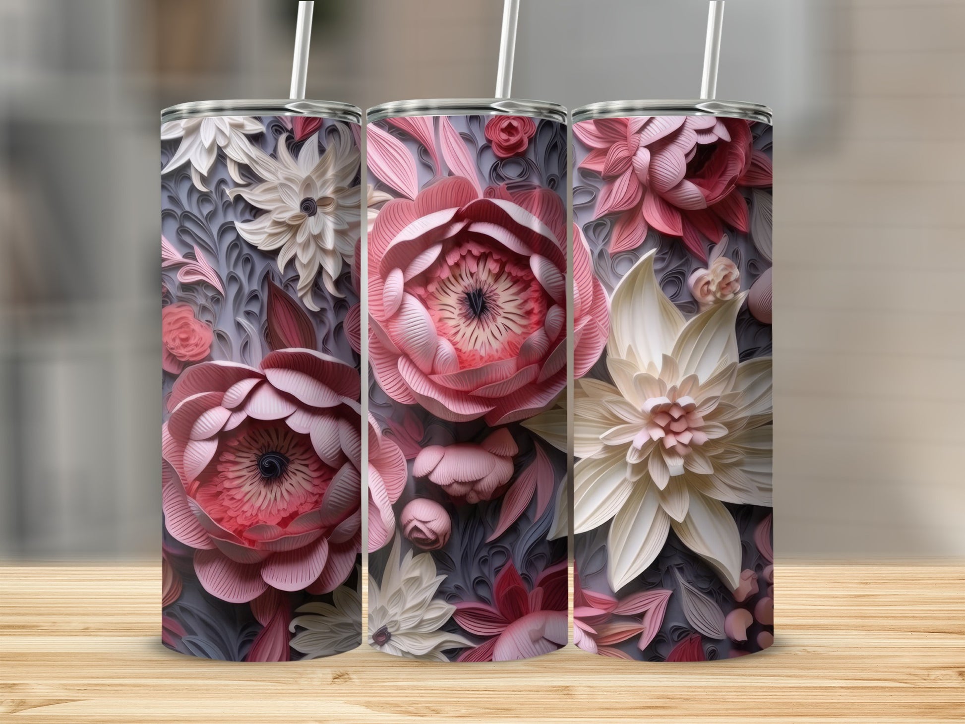 Three floral-patterned tumblers with straws on a wooden surface.