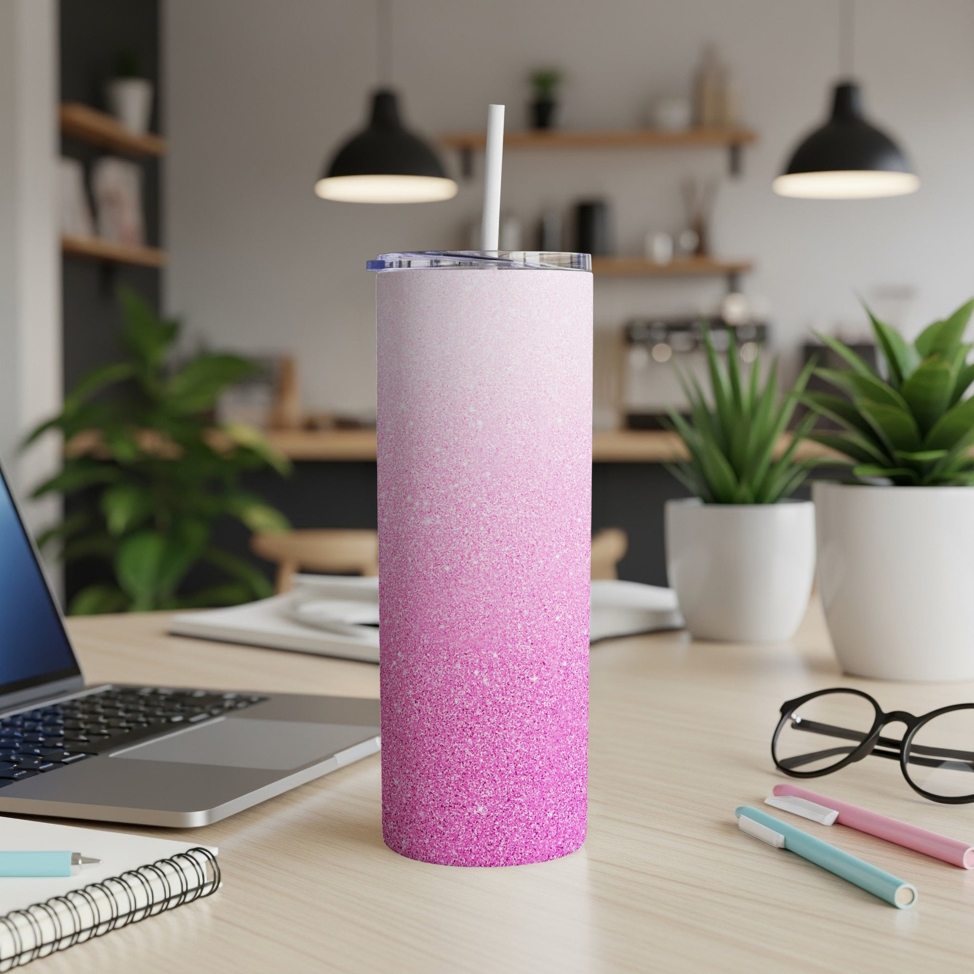 Pink glitter gradient skinny tumbler with straw on a desk.